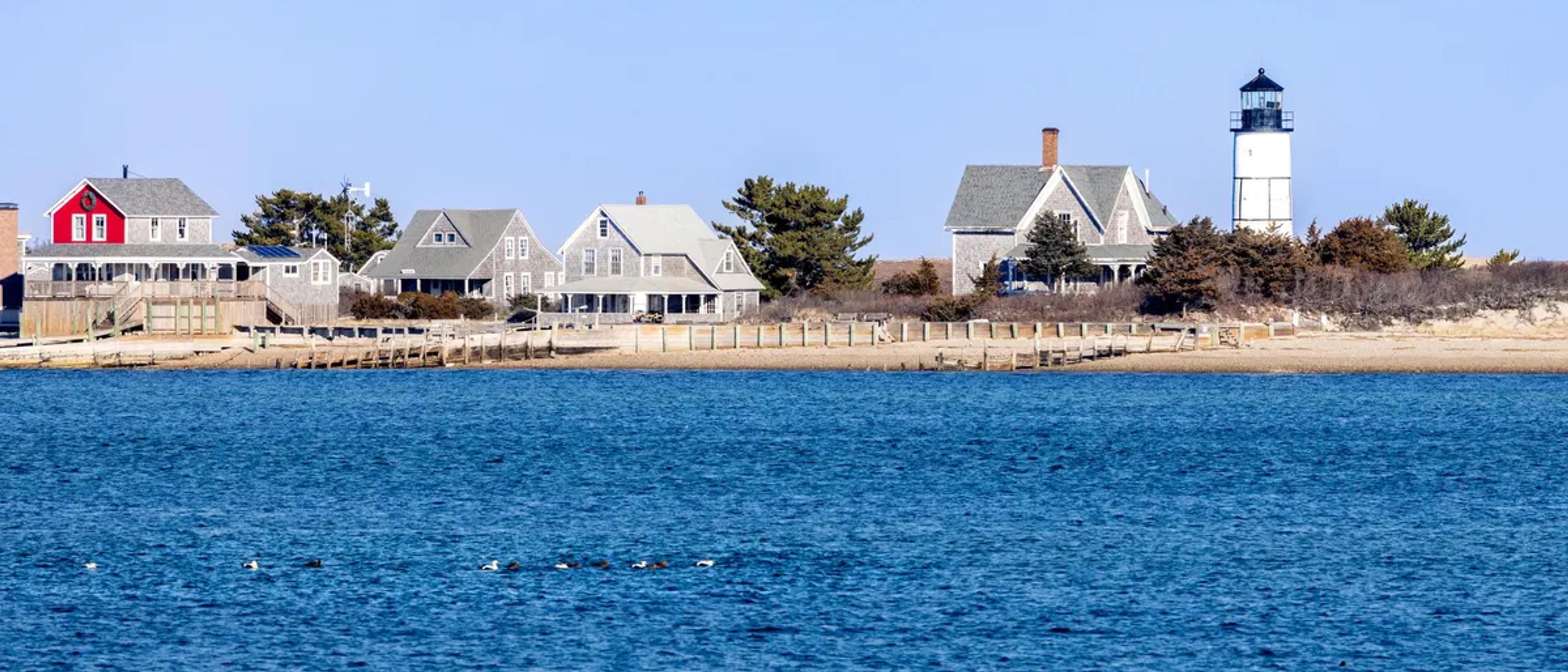 A row of New England seaside cottages and a lighthouse along the Cape Cod shore