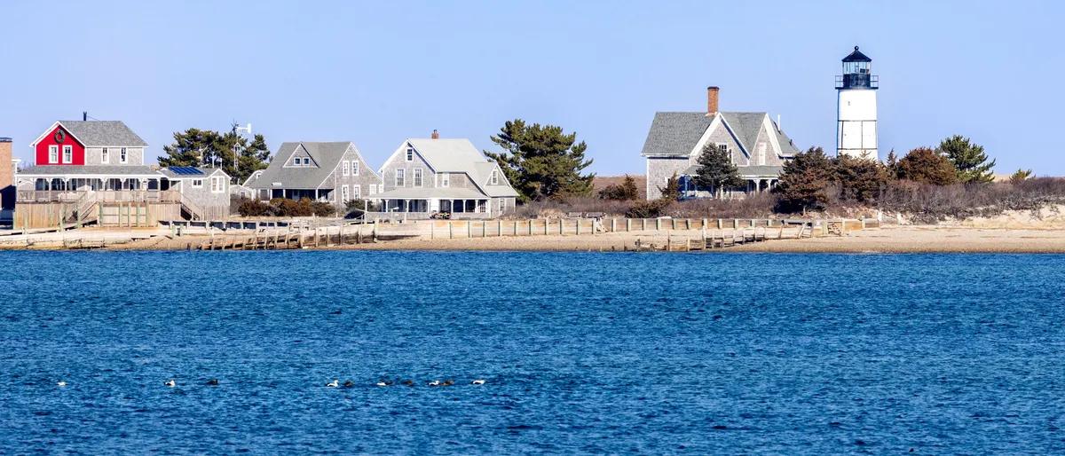 A row of New England seaside cottages and a lighthouse along the Cape Cod shore