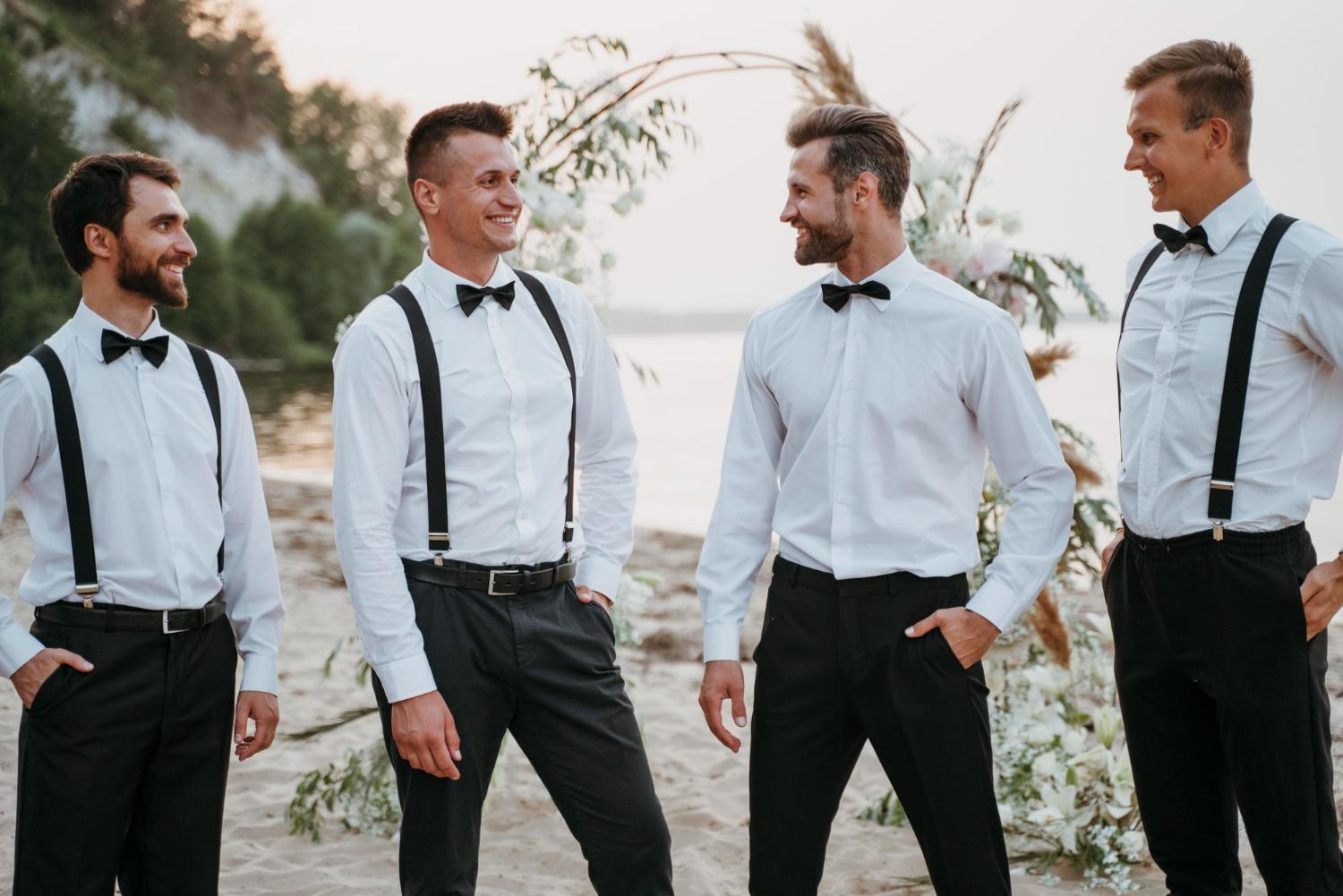 Vier gasten in wit overhemd met bretels en vlinderdas op een bruiloft aan het strand