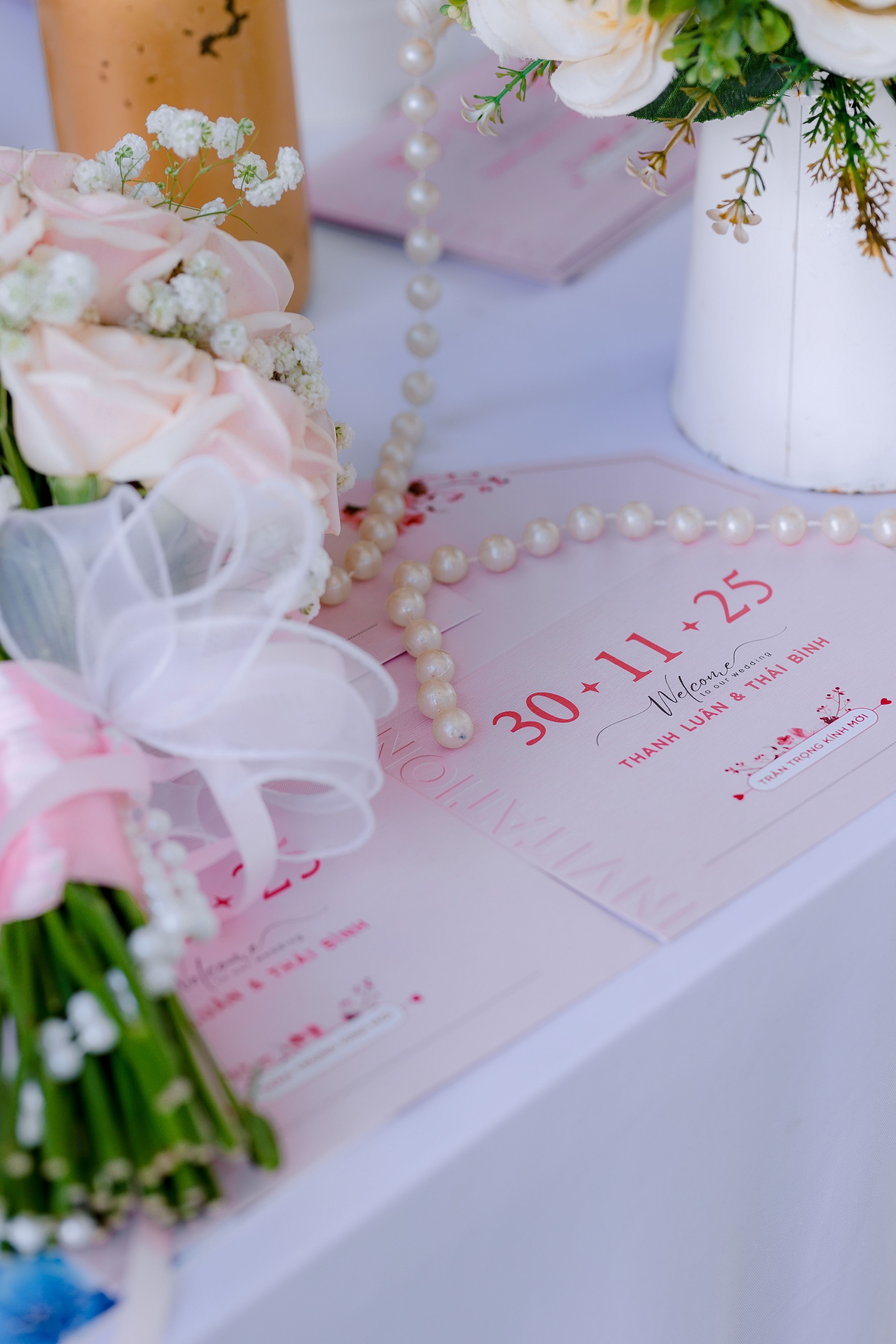 Roze trouwkaarten met een parelsnoer en een boeket rozen op tafel