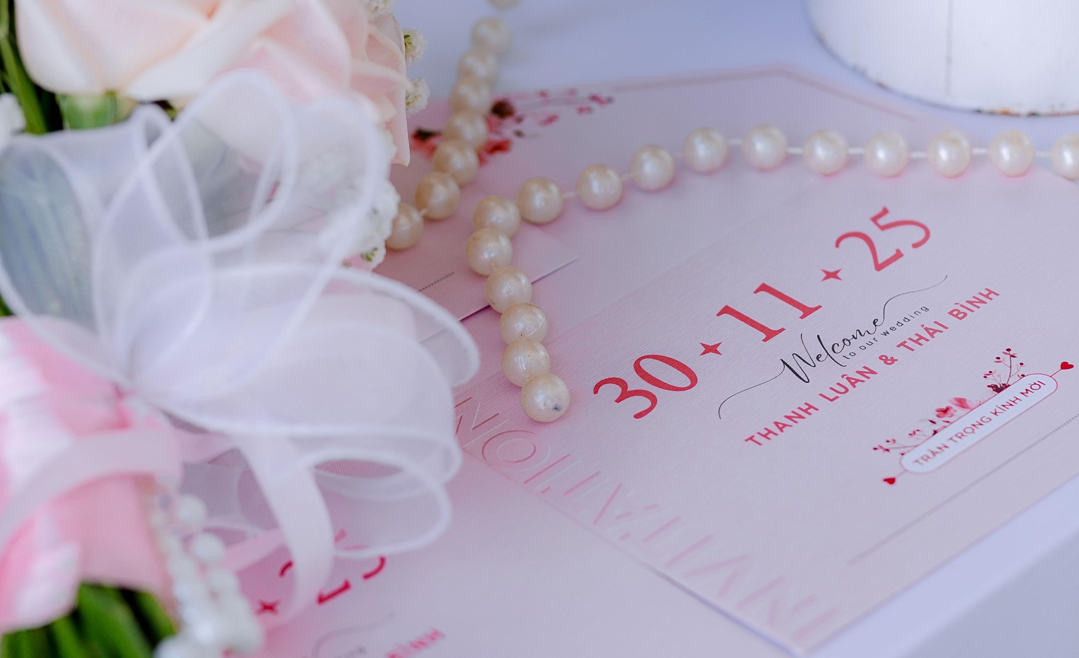 Roze trouwkaarten met een parelsnoer en een boeket rozen op tafel