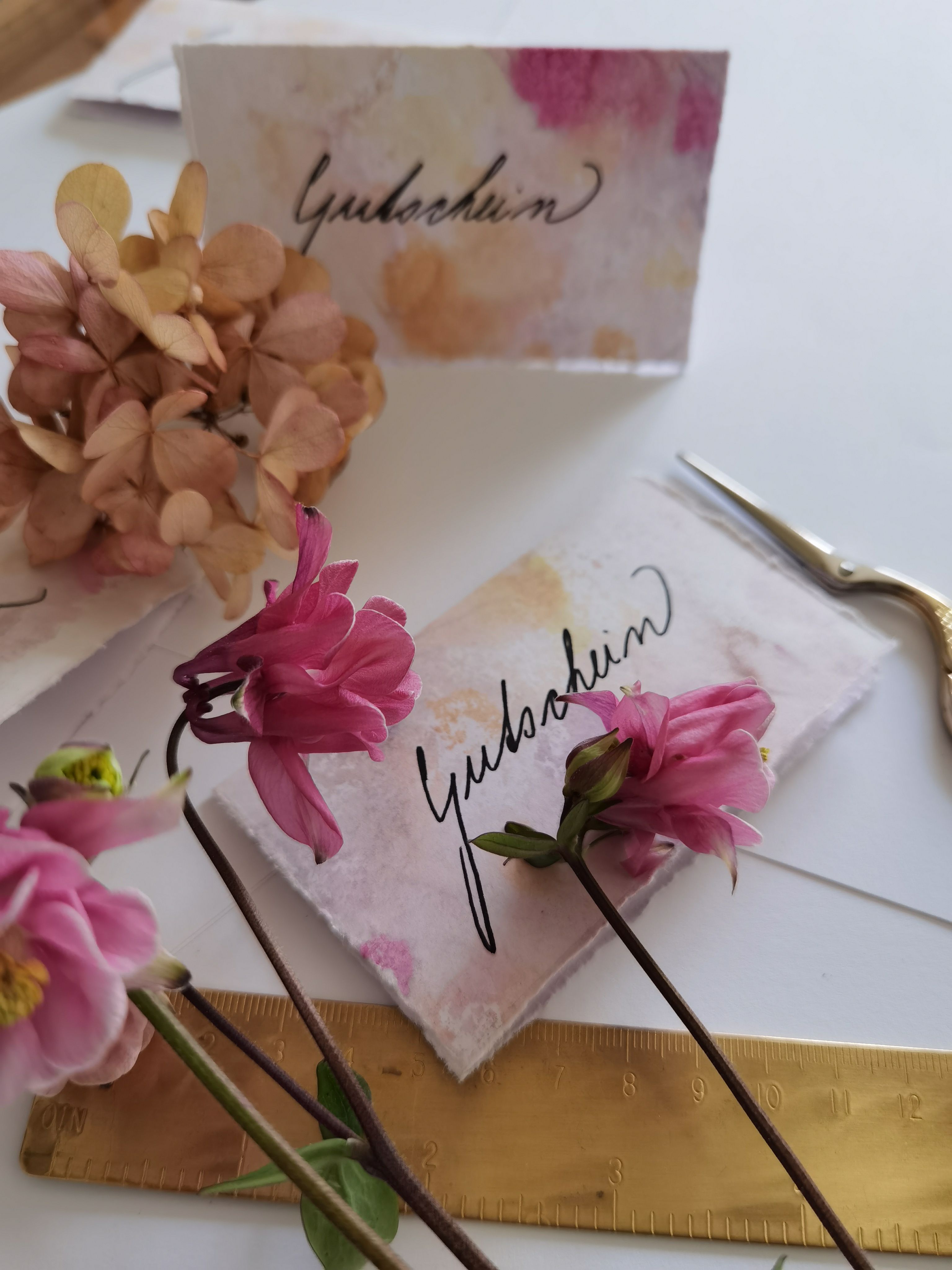 Handgeschreven naamkaartjes met bloemen, een schaar en een liniaal