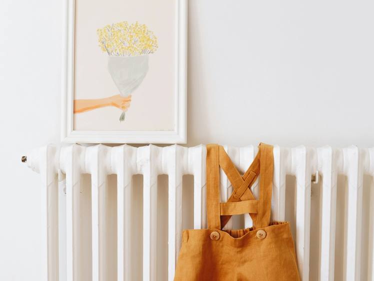 A child's mustard dungarees hanging on a radiator below a framed print