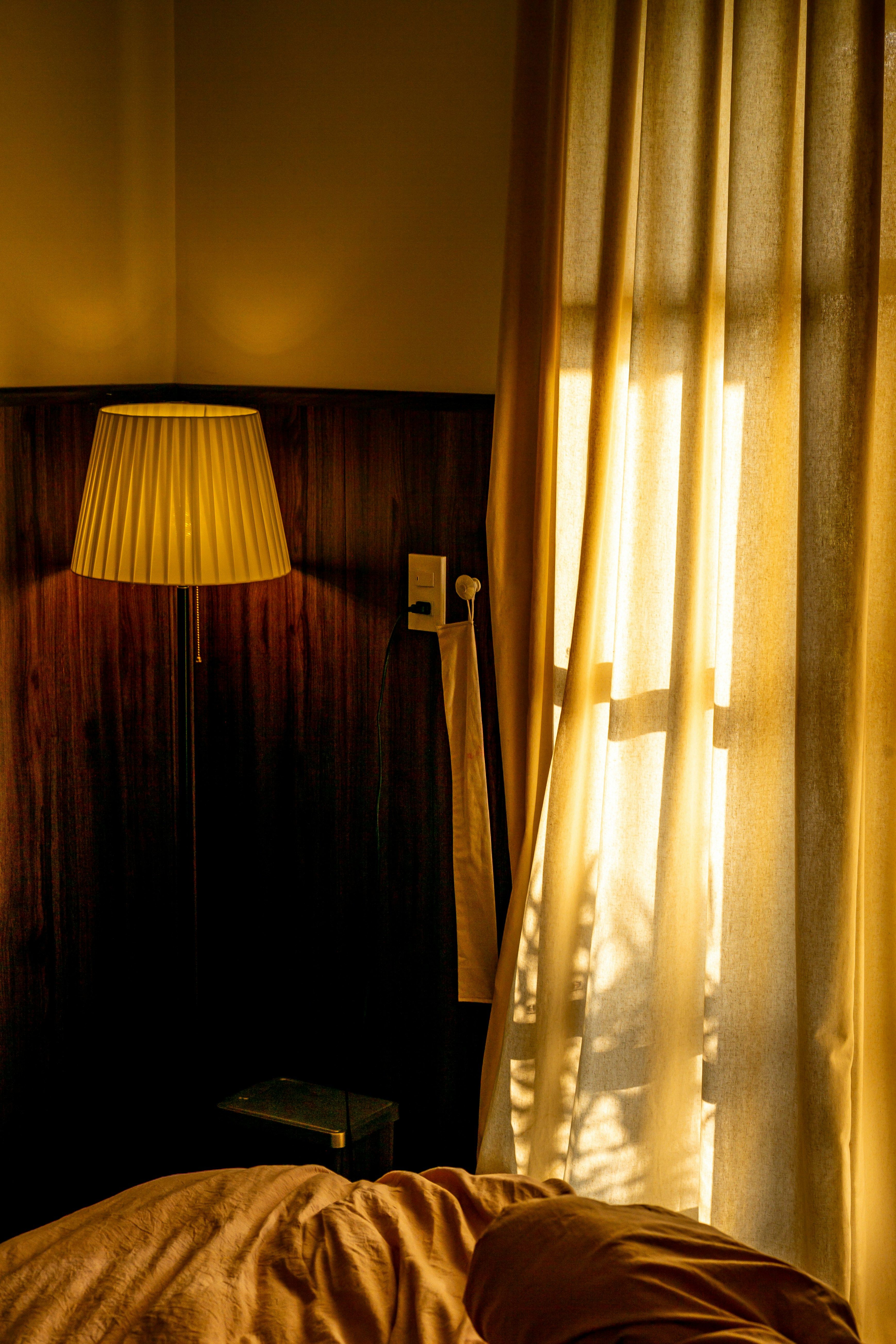 A bedroom at dusk lit by a single lamp, with sunlight through gold curtains