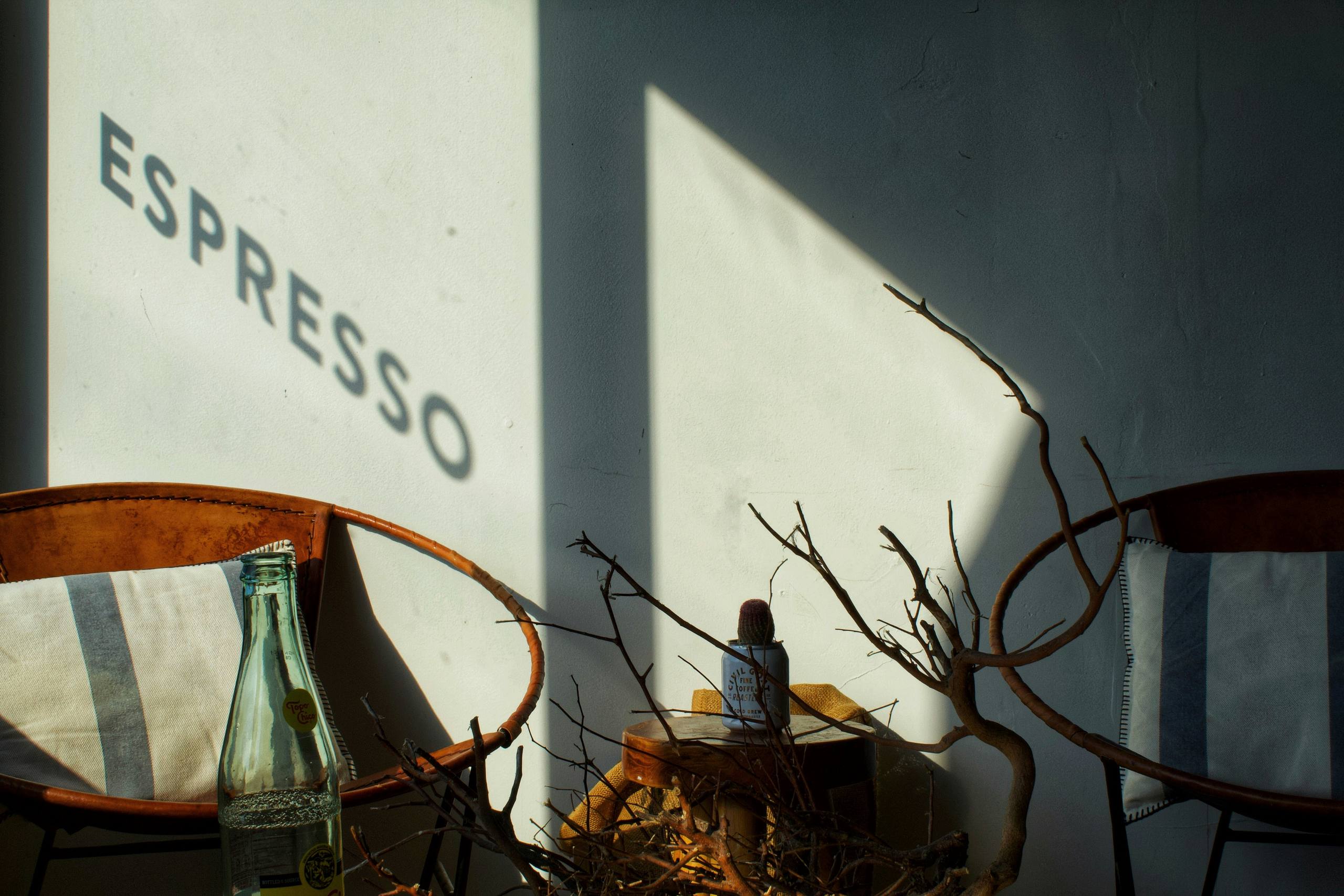 A wall painted with the word Espresso, above chairs and dried branches