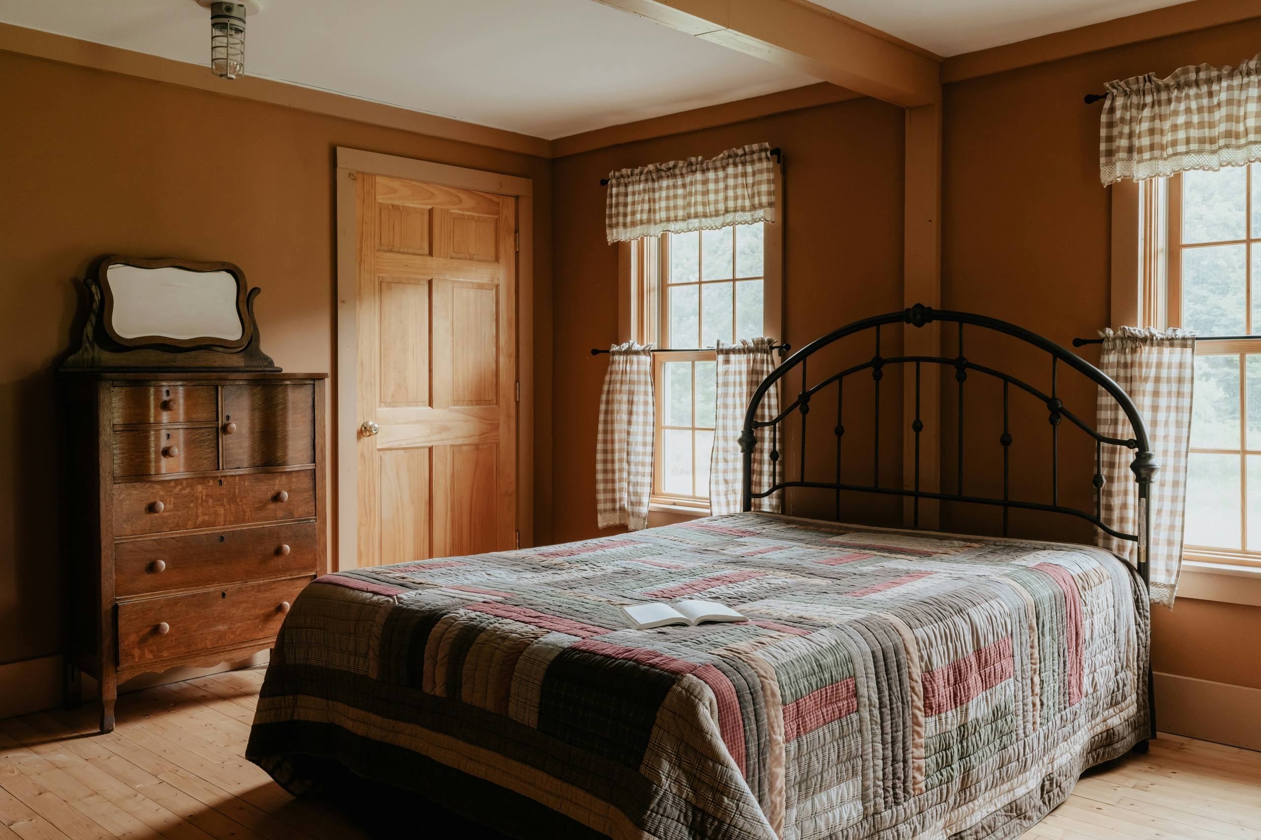 A bedroom with an iron bedstead, a patchwork quilt and a wooden chest of drawers
