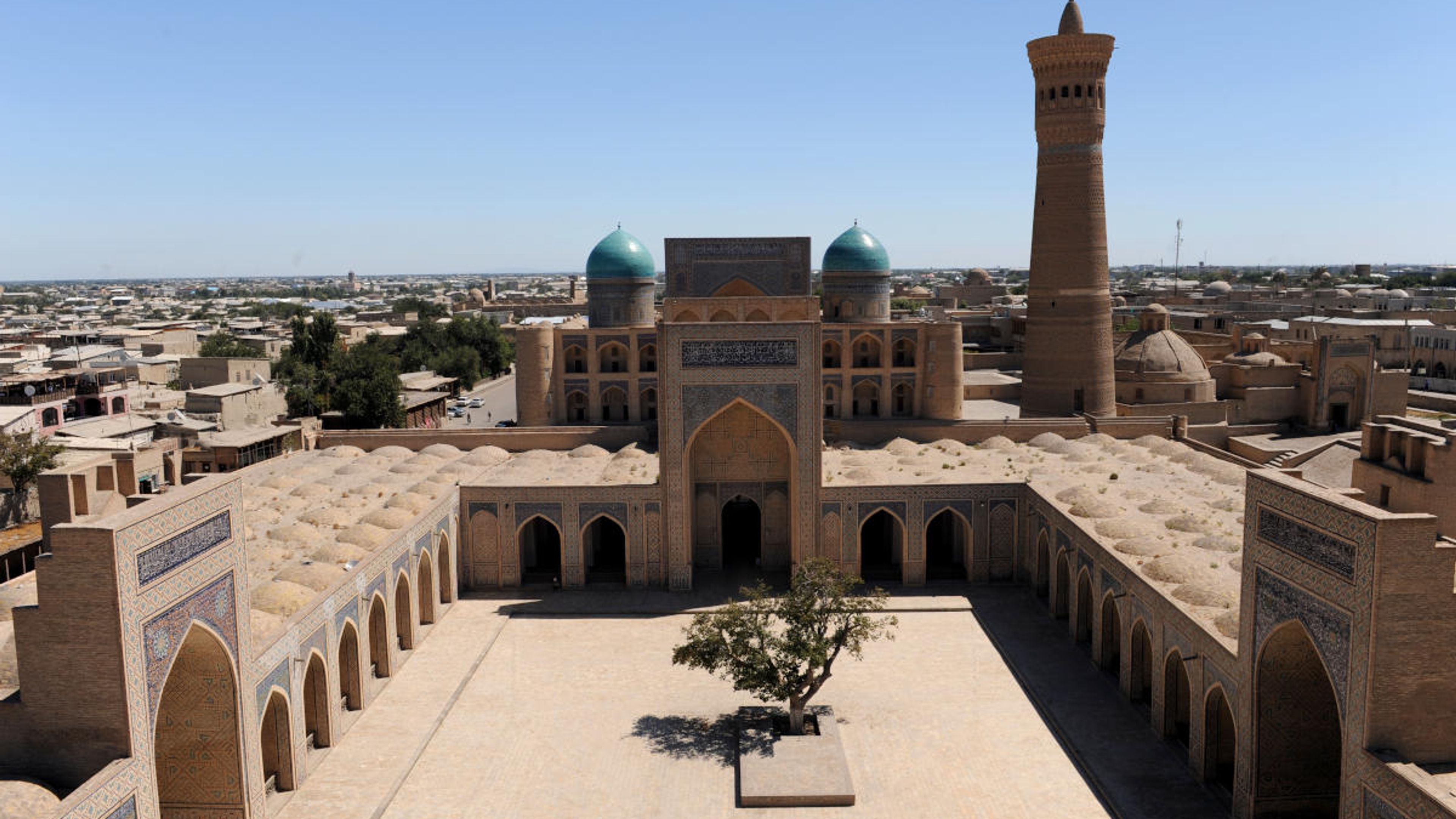 Blick in den Innenhof der Kalon Moschee in Buchara, Usbekistan, mit Minarett und blauen Kuppeln.