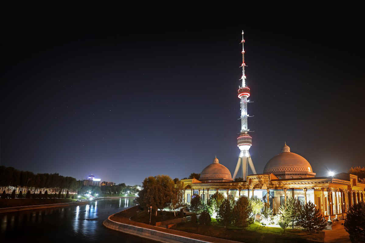 La Torre della Televisione di Tashkent illuminata in Uzbekistan di notte accanto a un edificio.