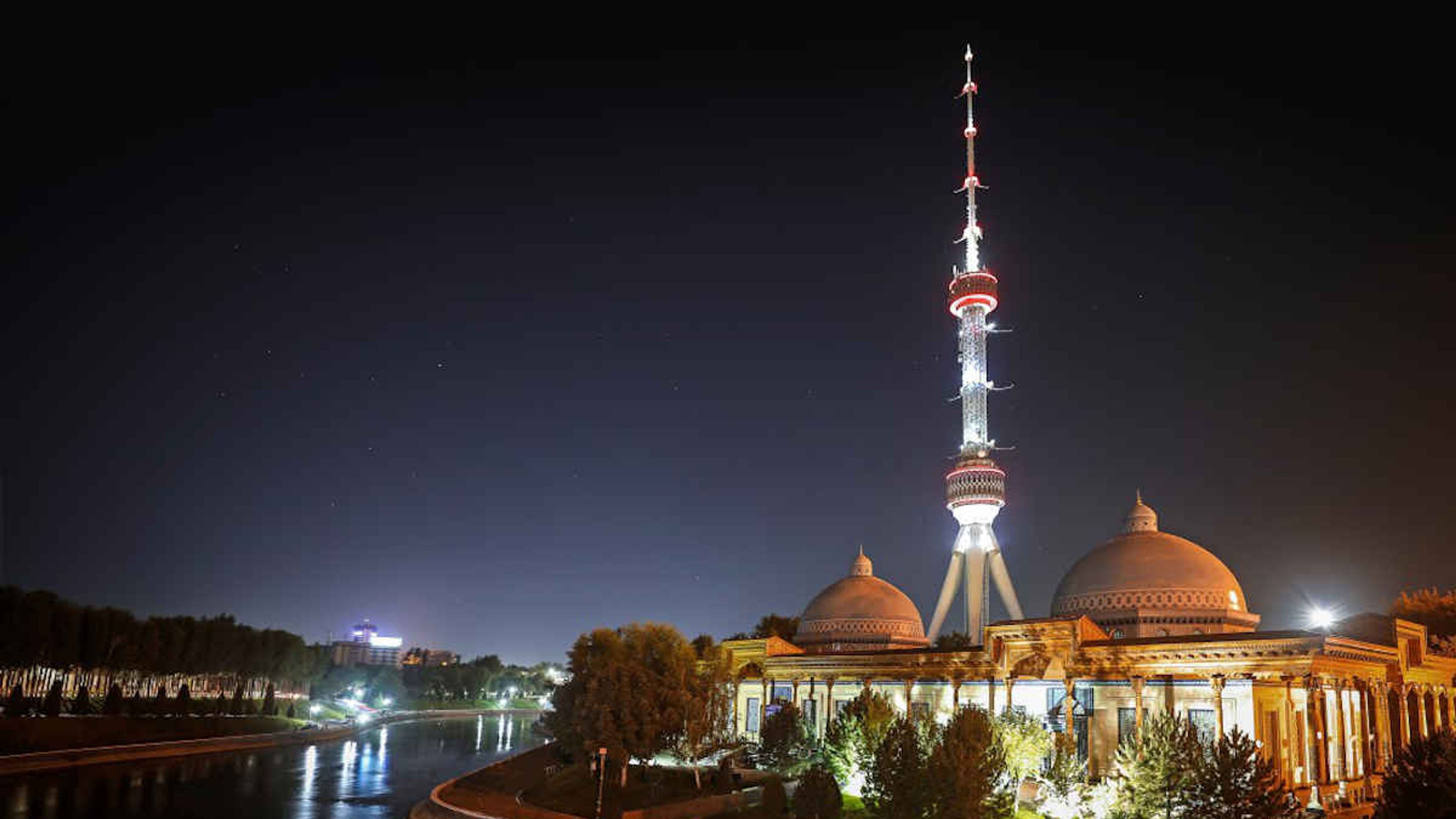 La Torre della Televisione di Tashkent illuminata in Uzbekistan di notte accanto a un edificio.