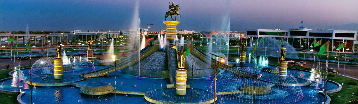 Monument de l'indépendance à Achgabat avec des fontaines illuminées et drapeaux du Turkménistan.