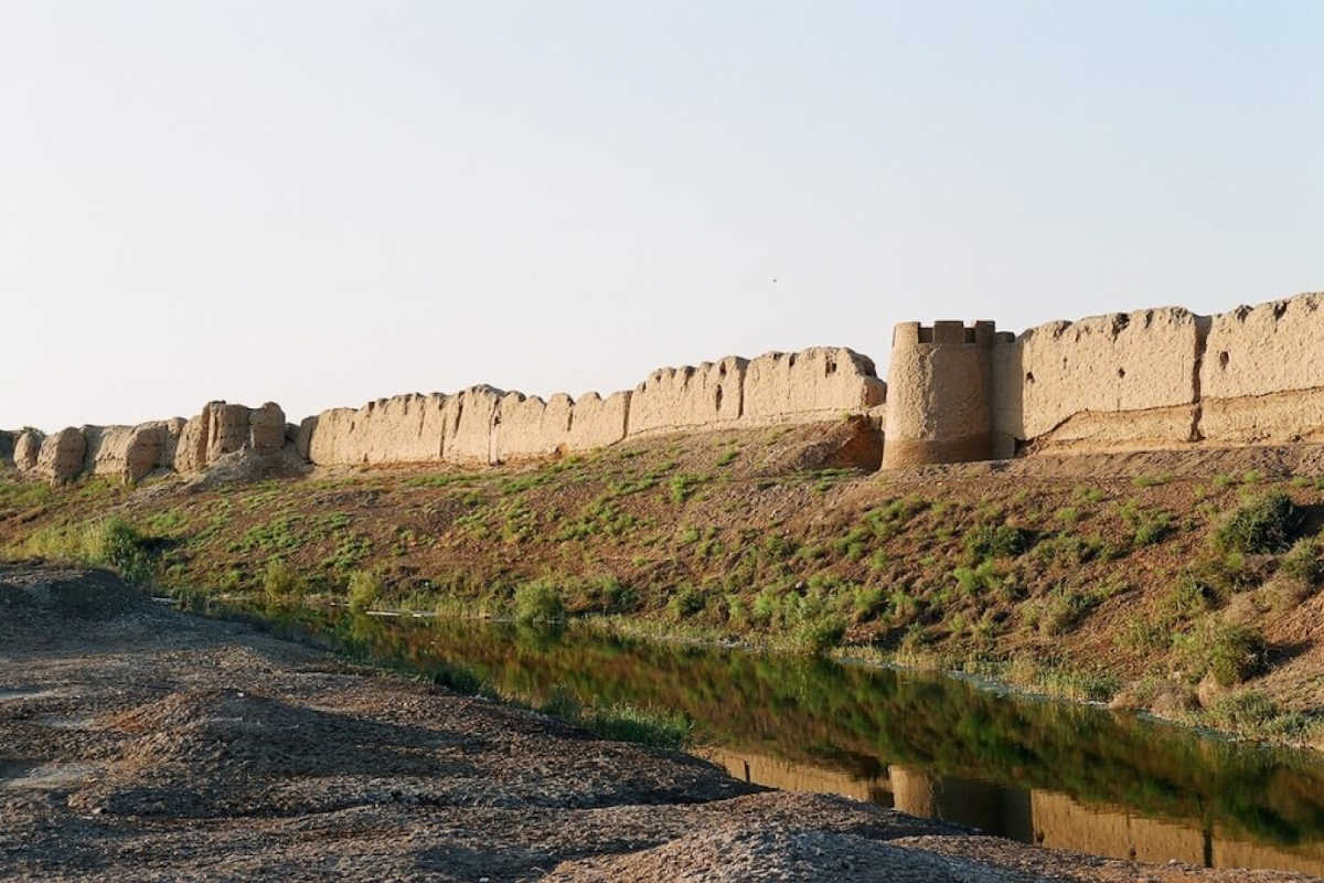 Anciens murs en pisé du site UNESCO de Merv au Turkménistan avec douves au premier plan.