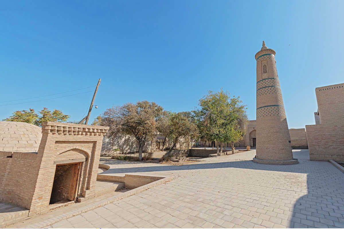 Madrasa Turt Shaffaz a Khiva, Uzbekistan: Punto di riferimento storico con minareto e cortile sotto il cielo azzurro.