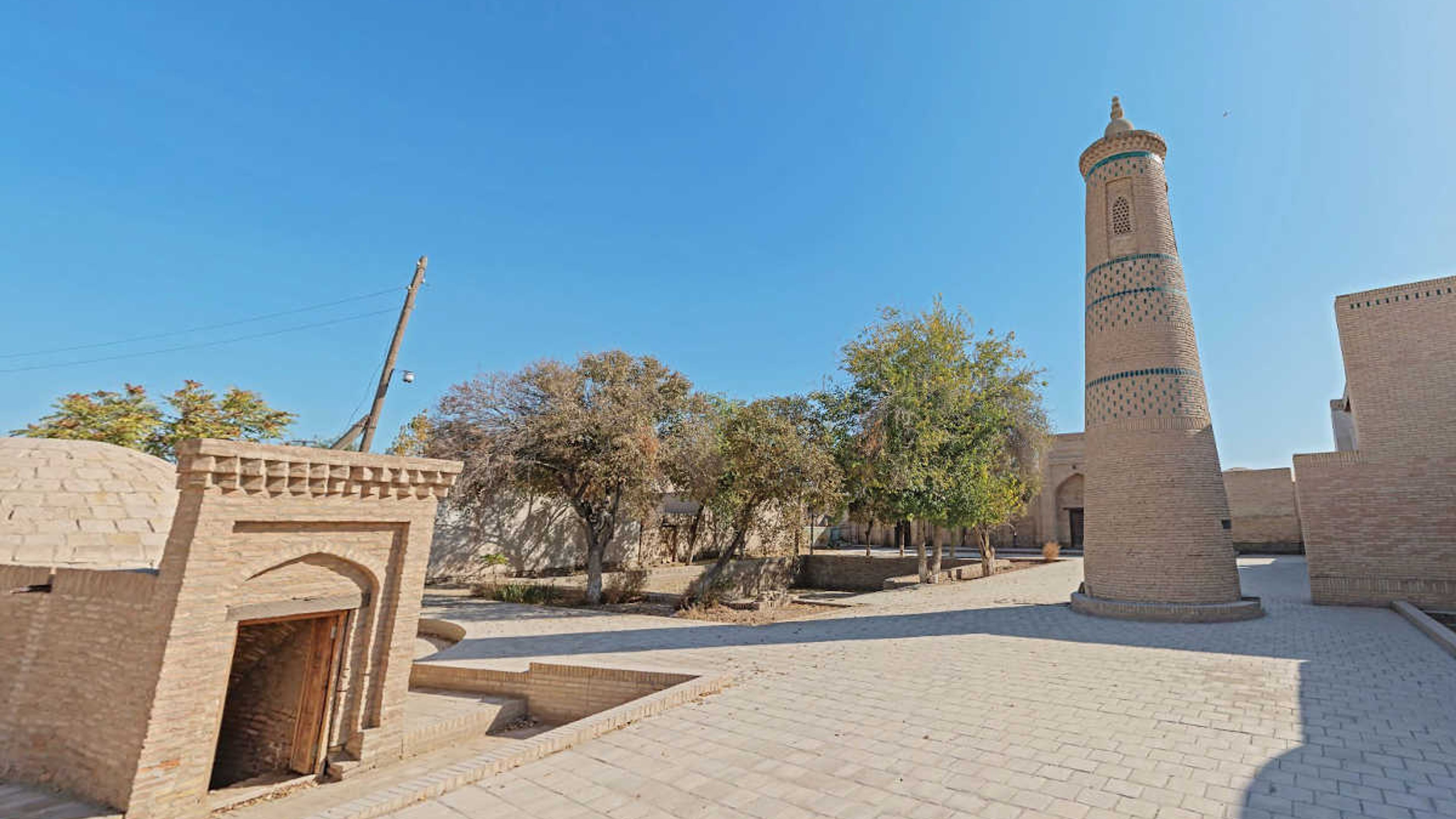 Madrasa Turt Shaffaz a Khiva, Uzbekistan: Punto di riferimento storico con minareto e cortile sotto il cielo azzurro.