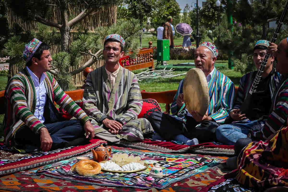 Uzbek men in traditional clothing and doppa hats playing music and having a picnic in Uzbekistan.