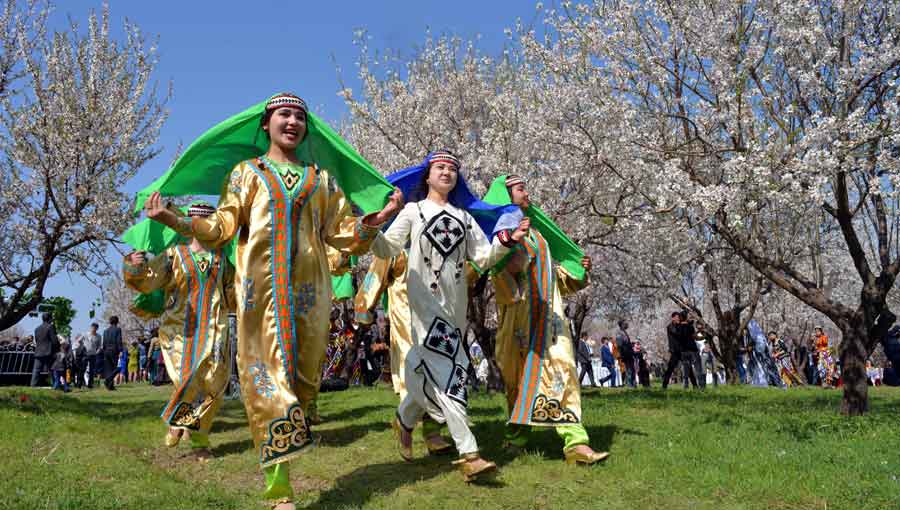 Women in traditional costumes dancing during the Nowruz spring festival under blooming trees in Central Asia.