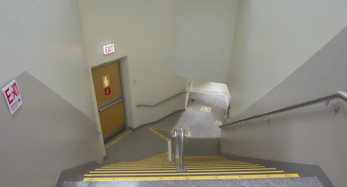 Empty modern school stairwell with emergency exit signage and multiple floor landings visible - Ark Strategic, Inc.