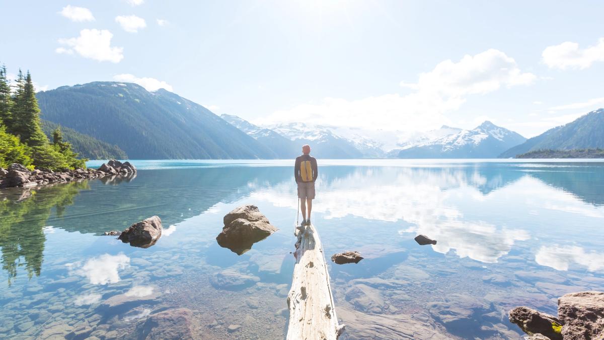 Man stands on the end of a log in a lake while looking out at a beautiful sunrise