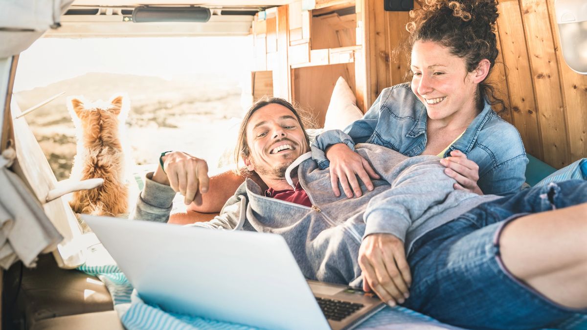 A hipster couple browse freelance jobs on their laptop from the back of their van