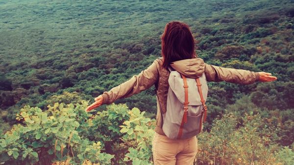 Woman spreads arms while standing on an overlook above a vast open forest