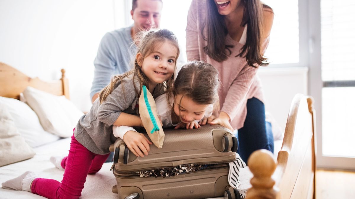 Mom and dad laugh while they pack a suitcase with two kids