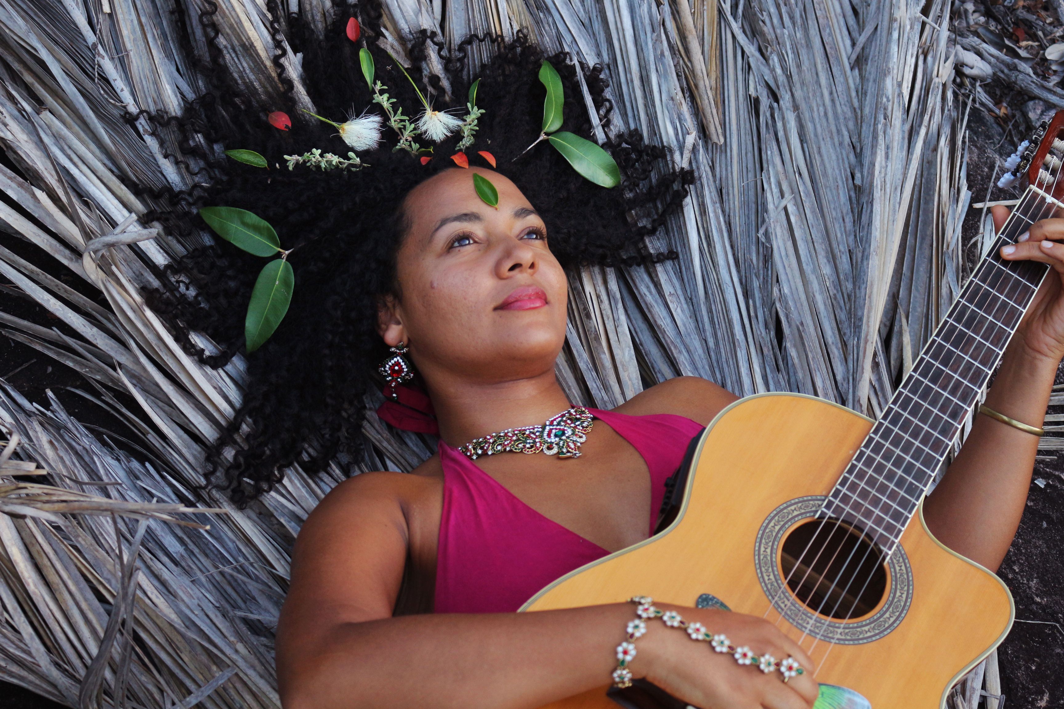 Andréa Cathalá tocando violão deitada e olhando o céu.
