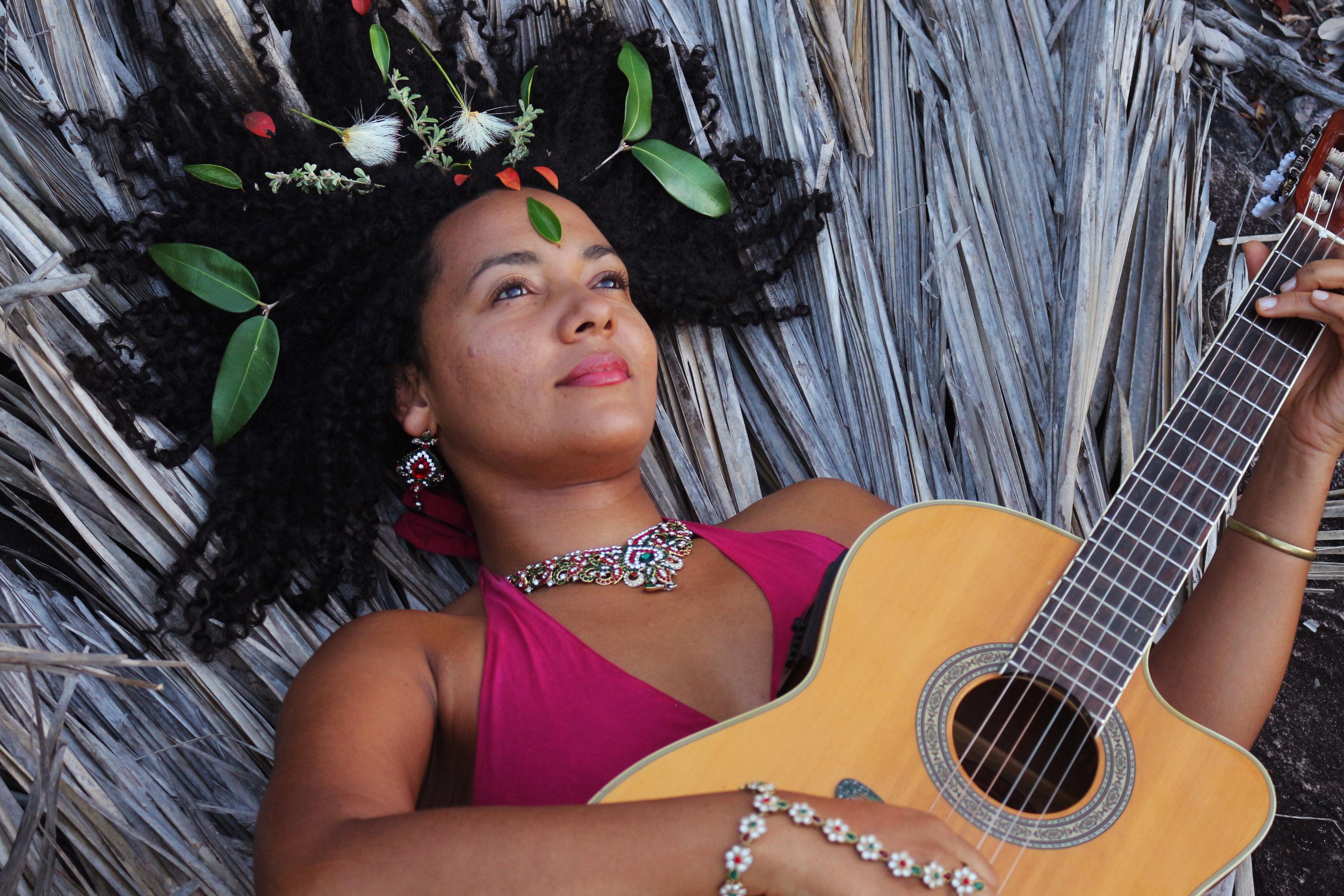 Andréa Cathalá tocando violão deitada e olhando o céu.