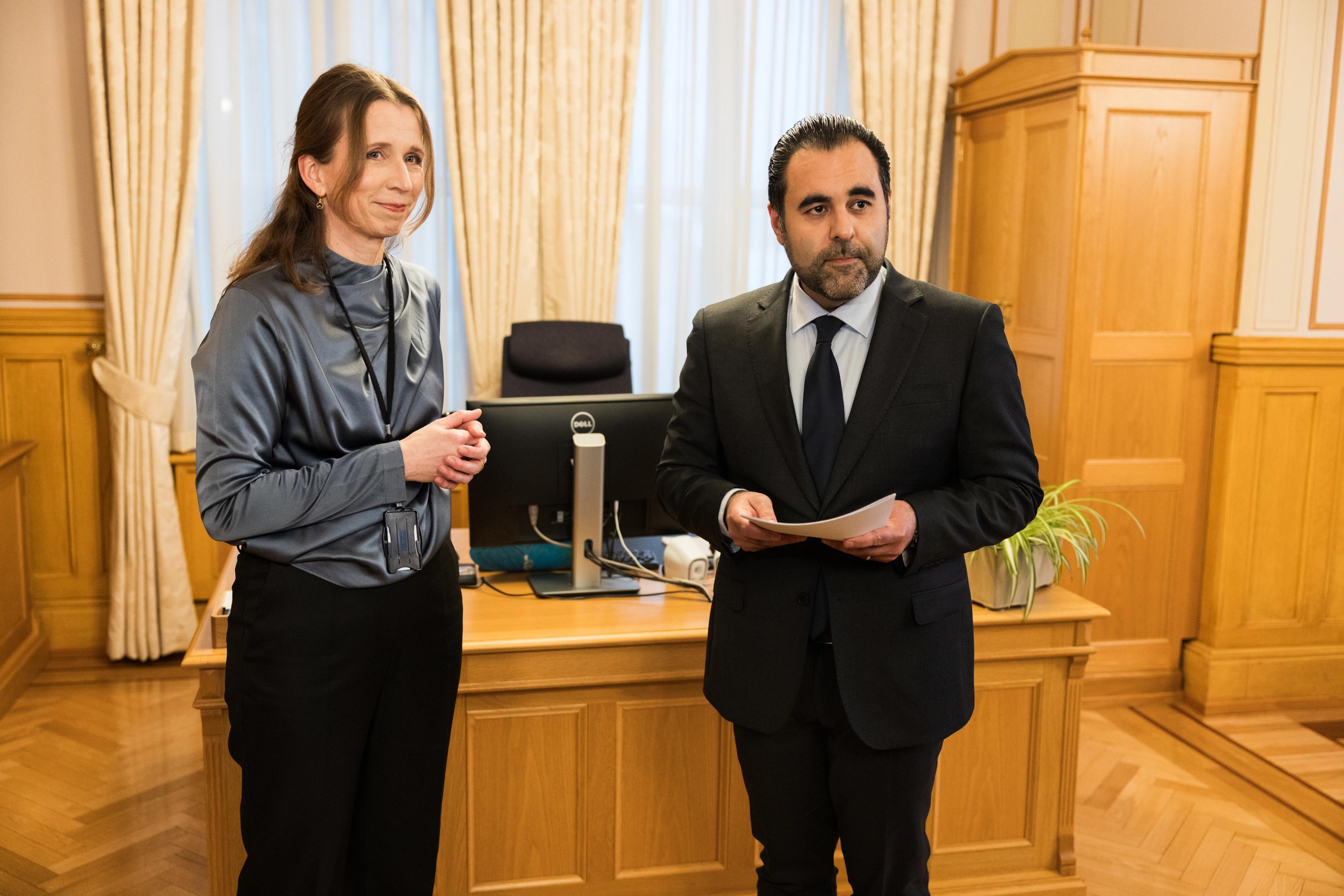 En kvinne og en mann inne på Stortinget. Mannen holder en rapport i hånda.