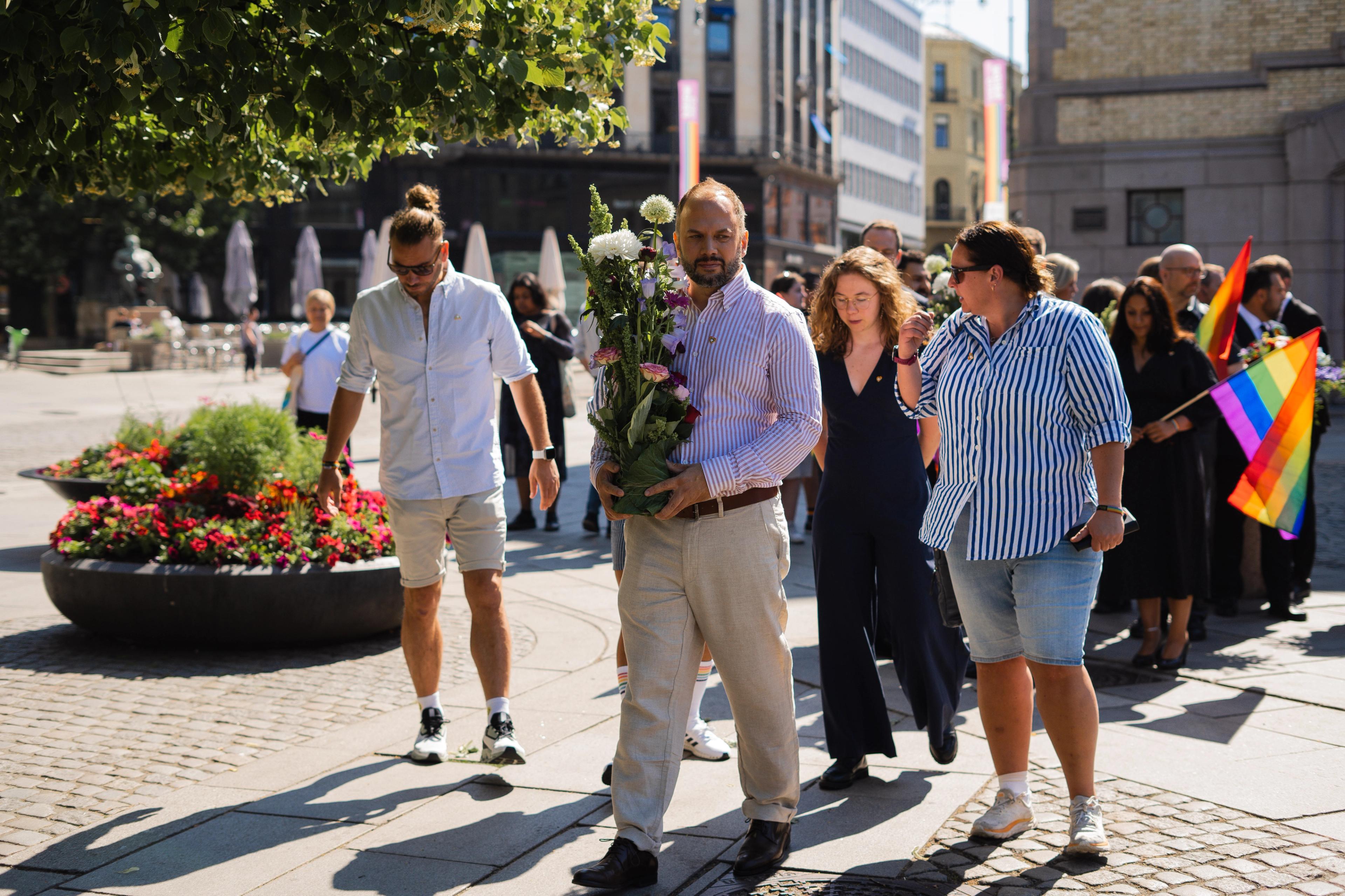 En gruppe mennesker går i tog. En mann holder blomster. Regnbueflagg kan ses i bakgrunnen.