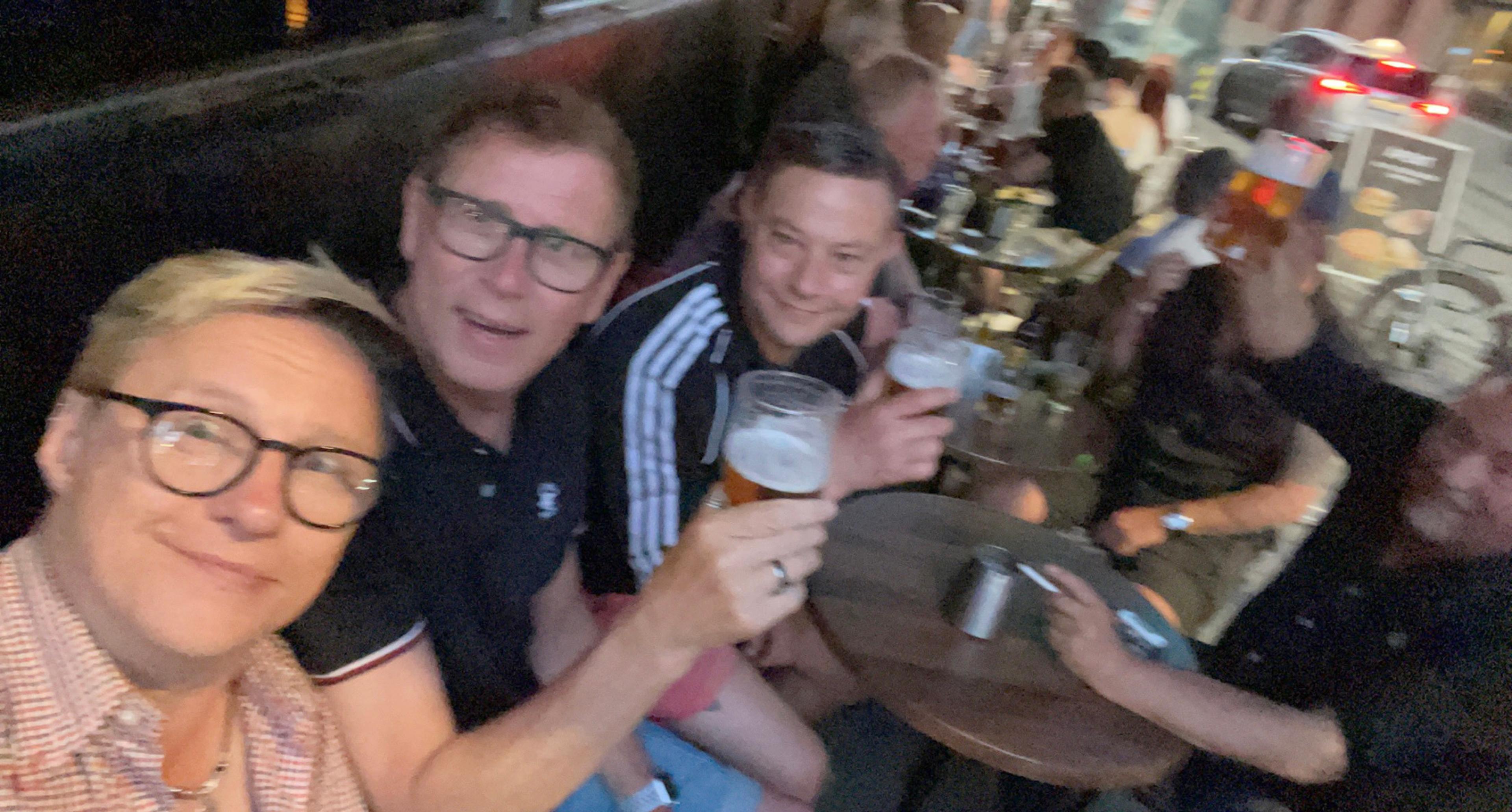 Bildet viser uteserveringen på Per på hjørnet. Fire menn smiler og ser i kameraet, og løfter ølen til en skål.