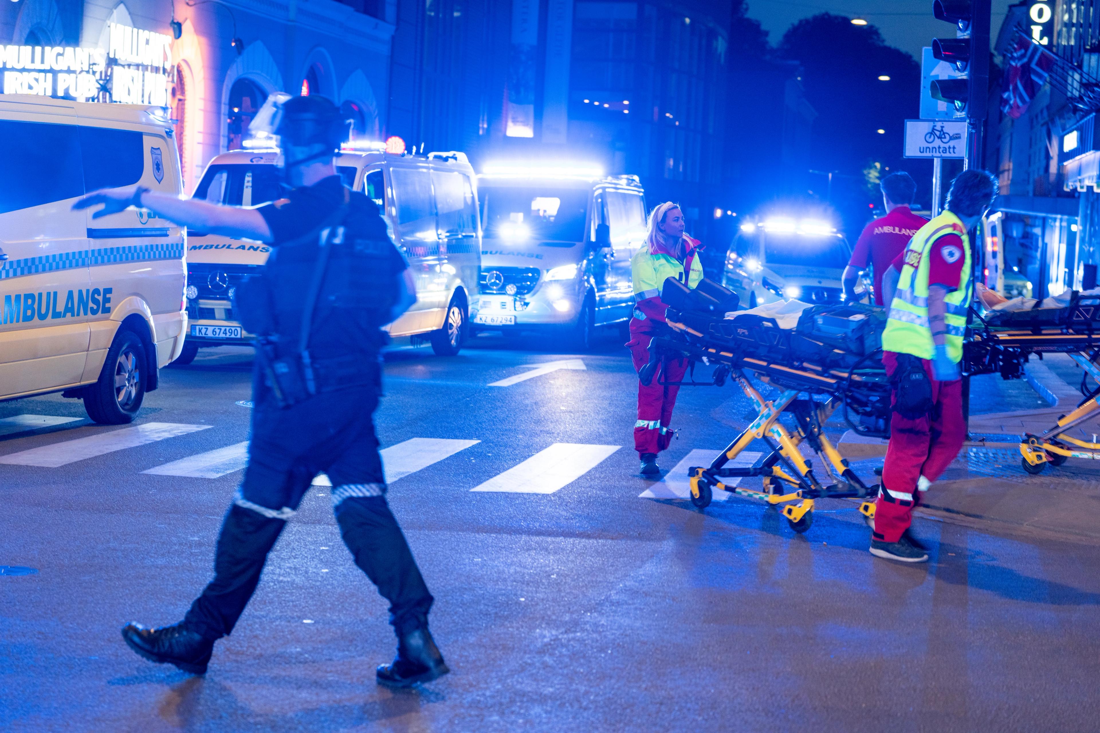 En rad med ambulanser står i gata. Flere ambulansearbeidere triller på bårer, og en politimann gir anvisninger.
