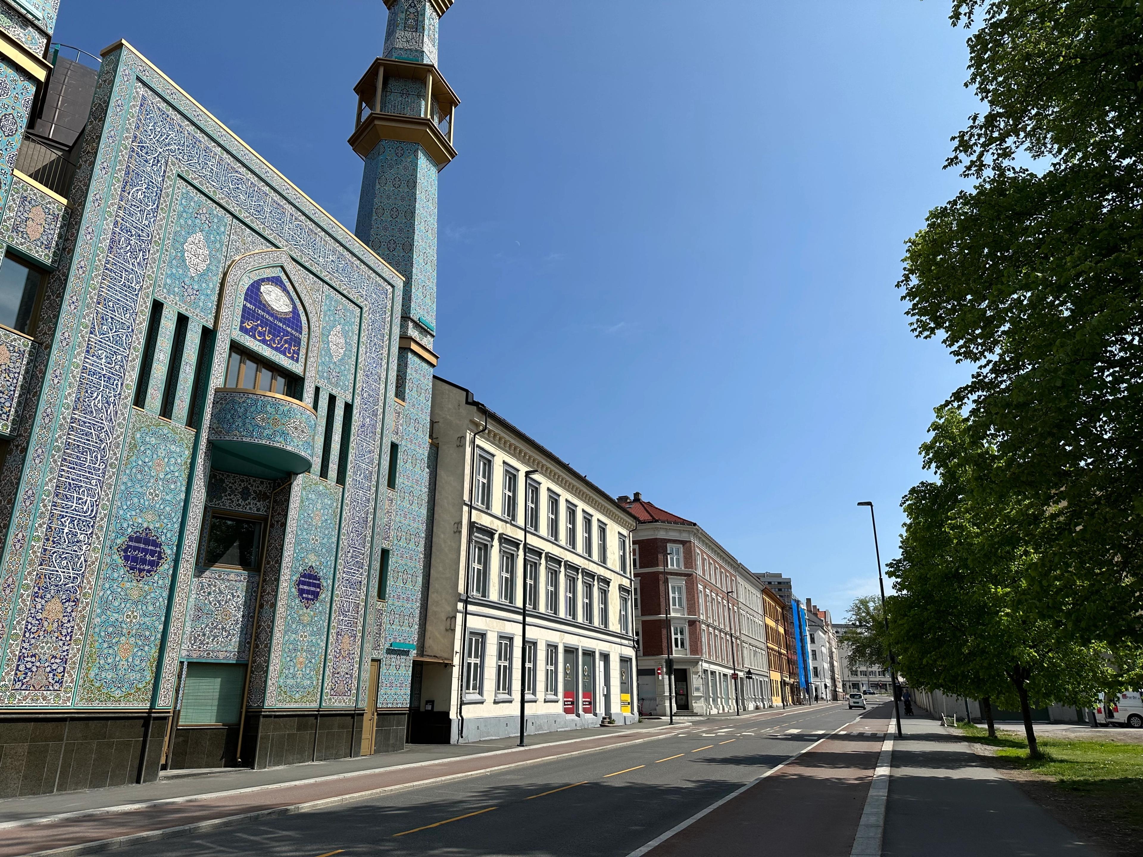 Bildet viser fasaden på en moské med blå mosaikk og minareter mellom klassiske bygårder i Oslo.