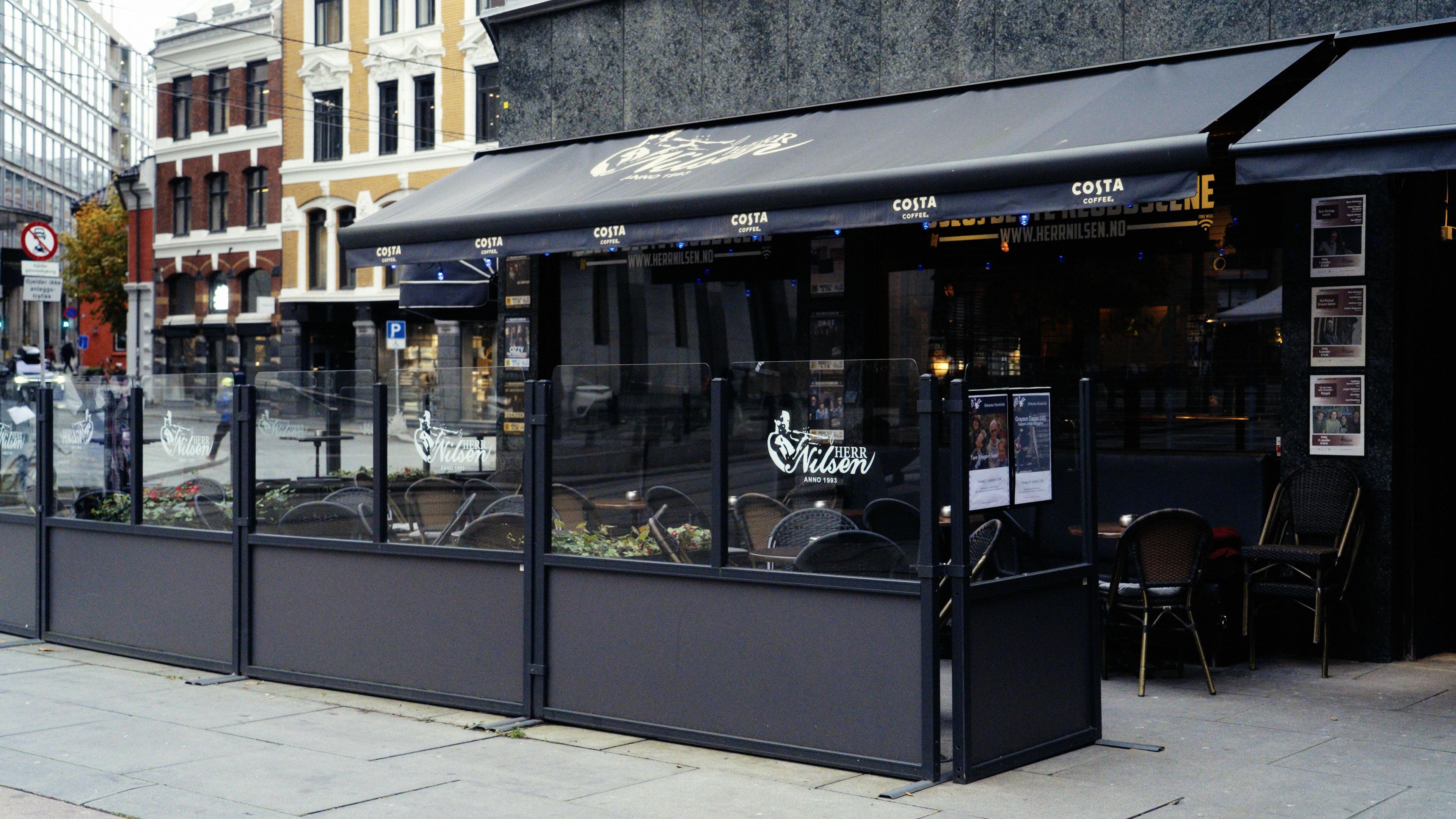 Fasaden på Herr Nilsen med stoler og bord på uteserveringen, og plakater for konserter ved døra.
