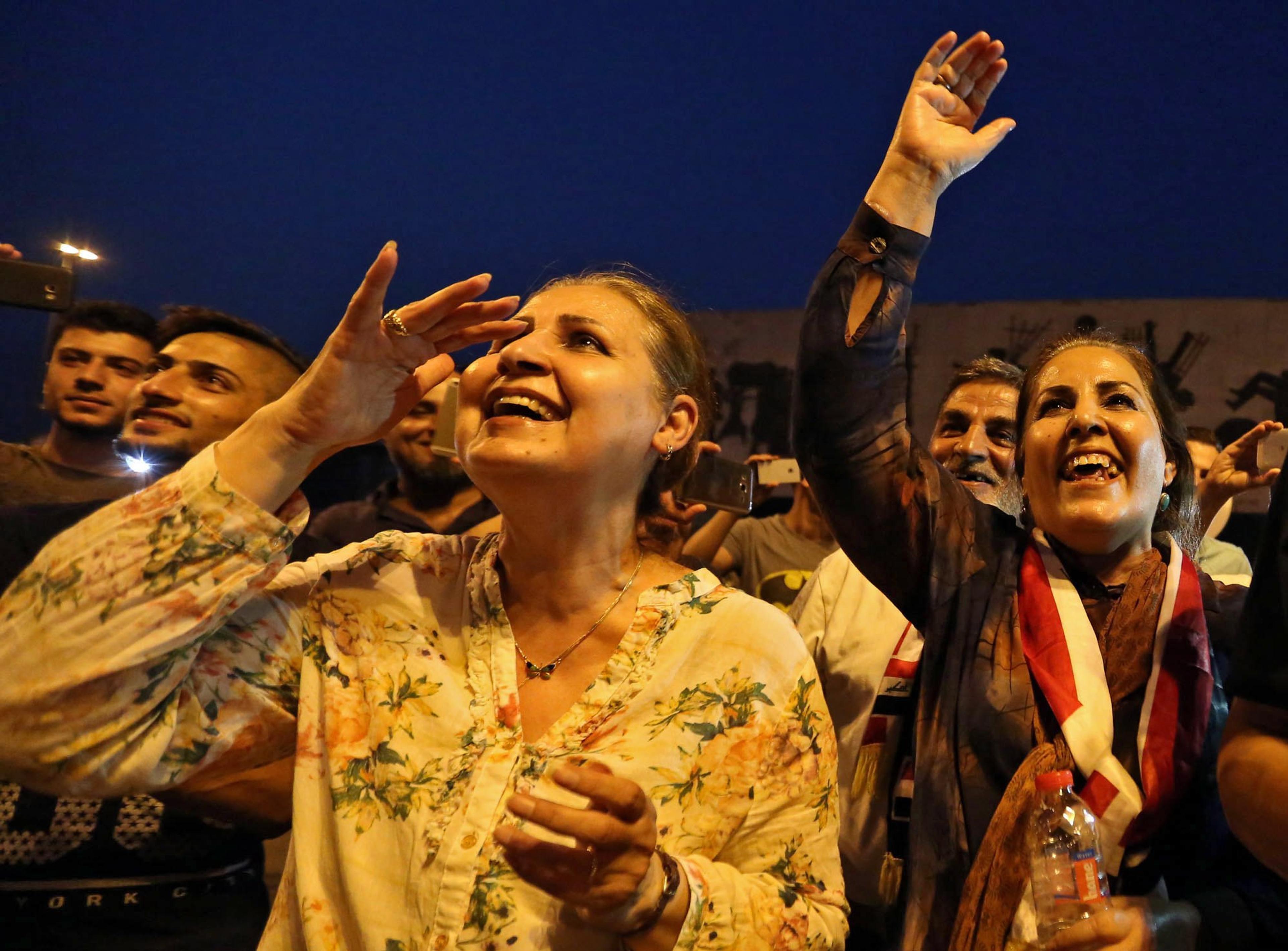 En folkemengde feirer i skumringen. To kvinner står i front og smiler.