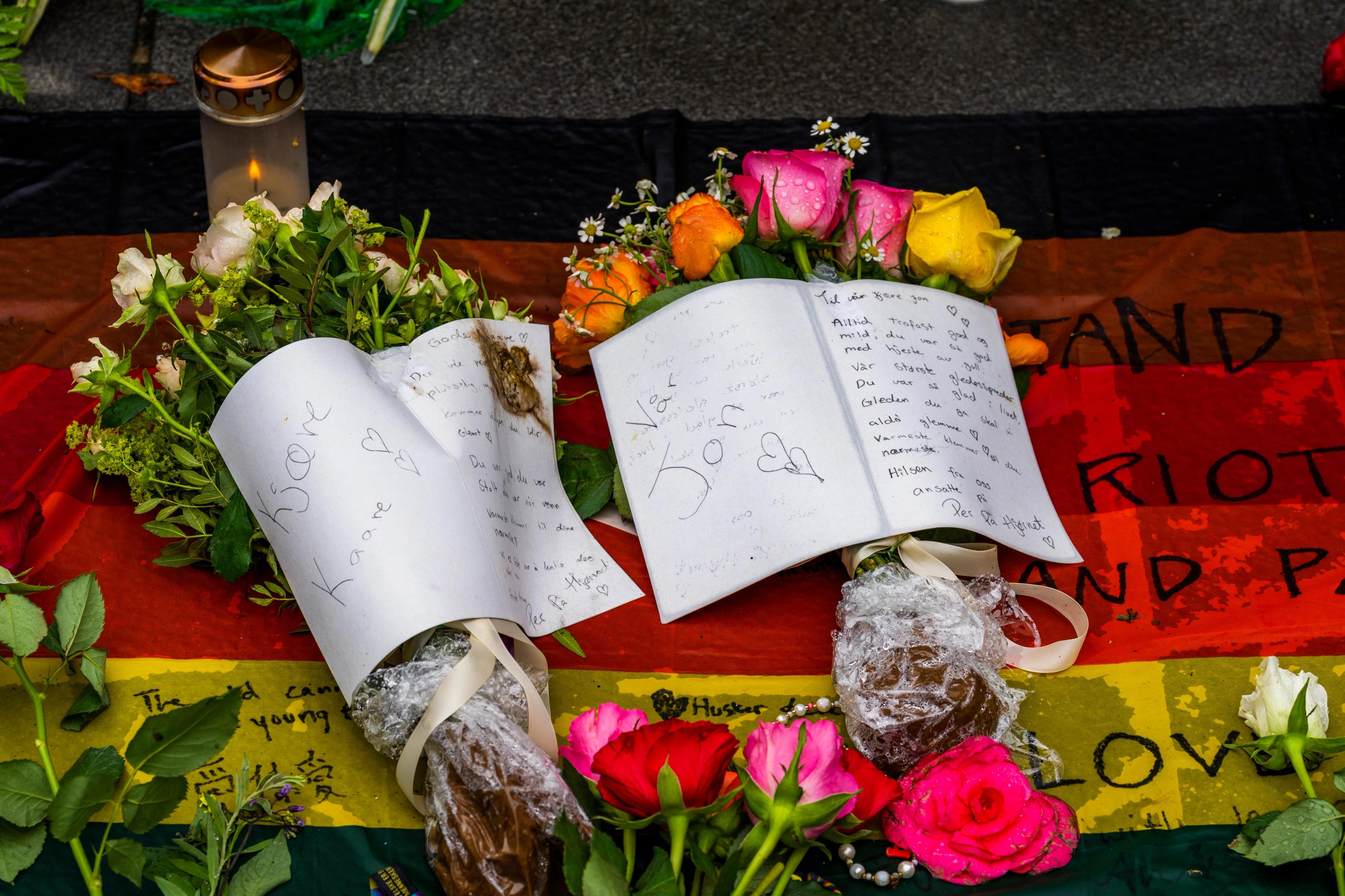 Kort til Kåre Arvid Hesvik og Jon Erik Isachsen som ble drept i angrepet, fra ansatte på Per på hjørnet. Kortene ligger oppå hver sin blomsterbukett og et pride-flagg.