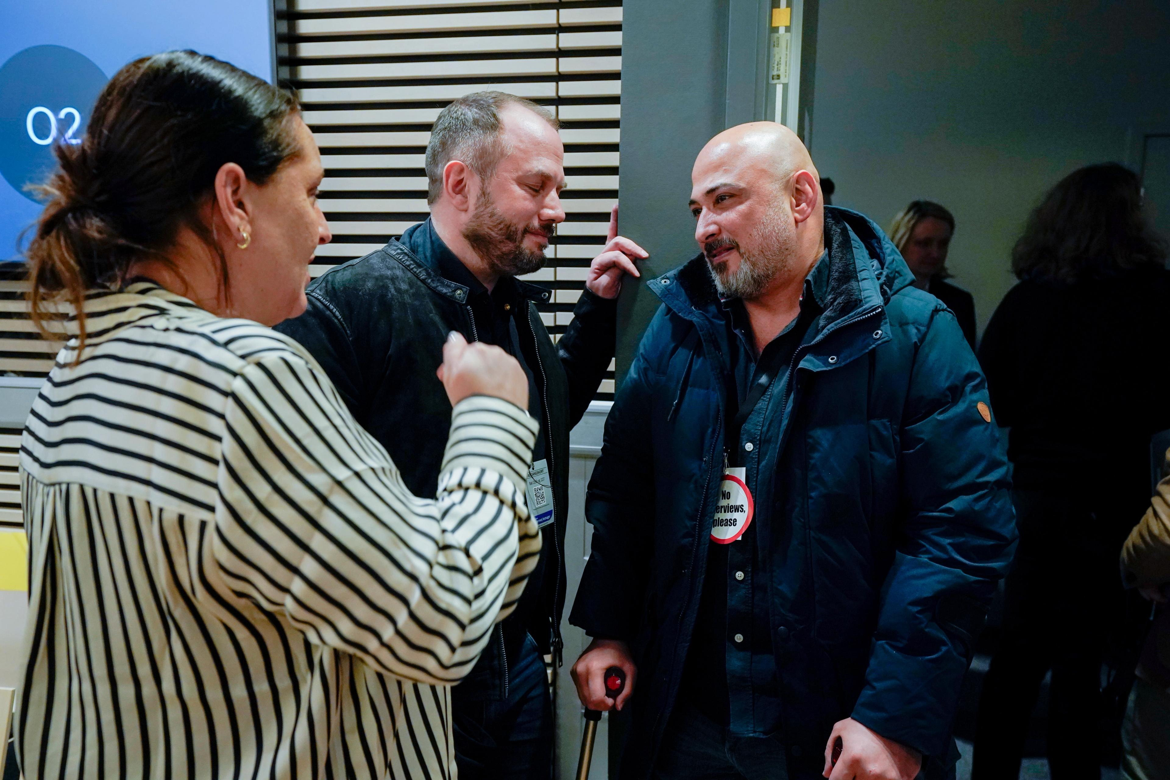 Tre fornærmede står og snakker med hverandre i rettssalen i en pause.