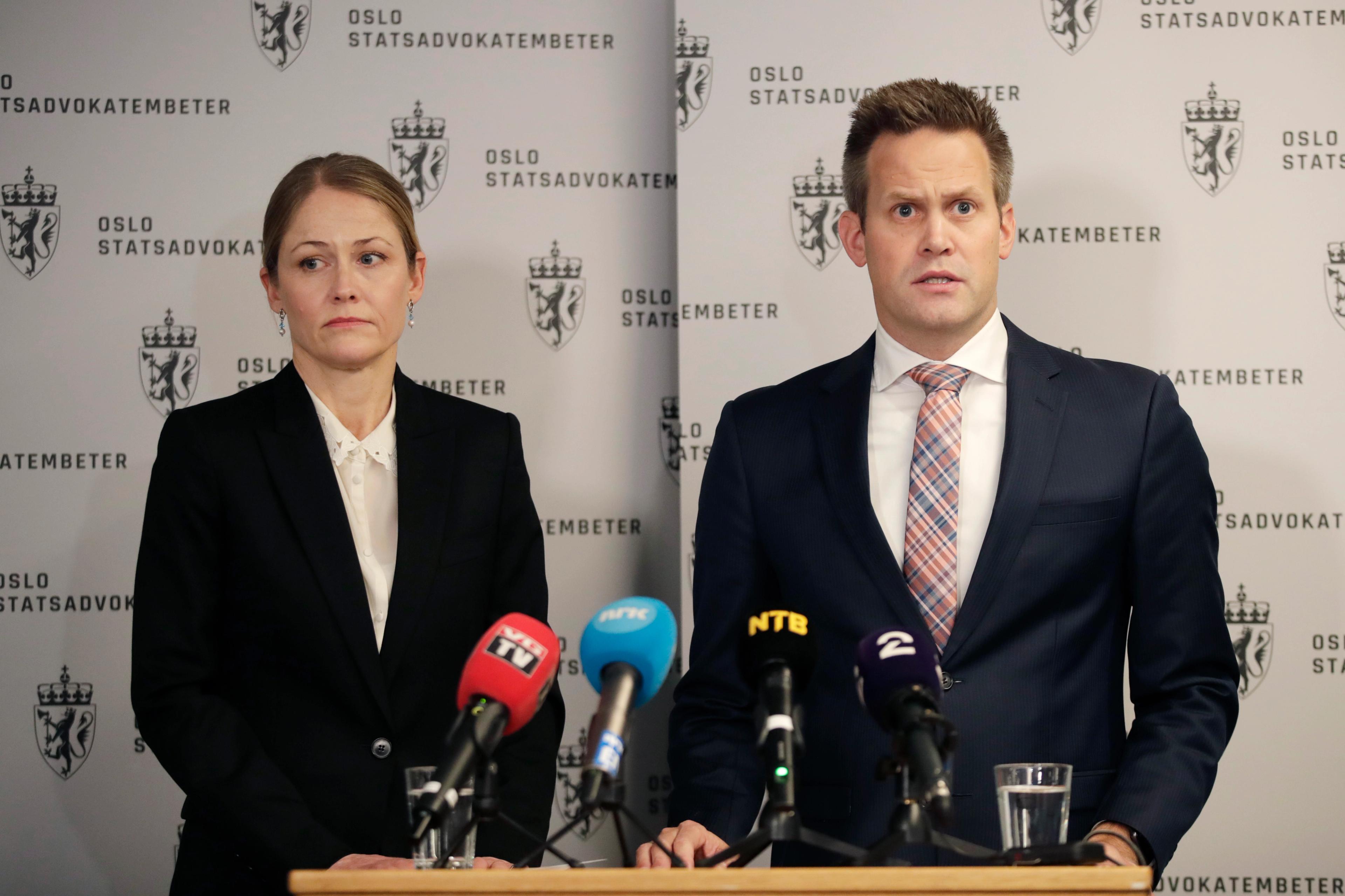 En mann og en dame står foran et bord med mikrofoner fra media.