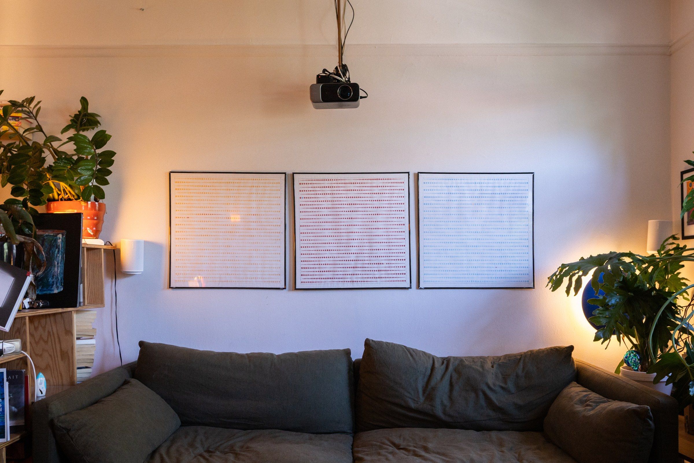 Translucent dot drawings framed and hung in a row on a wall above a dark sofa.