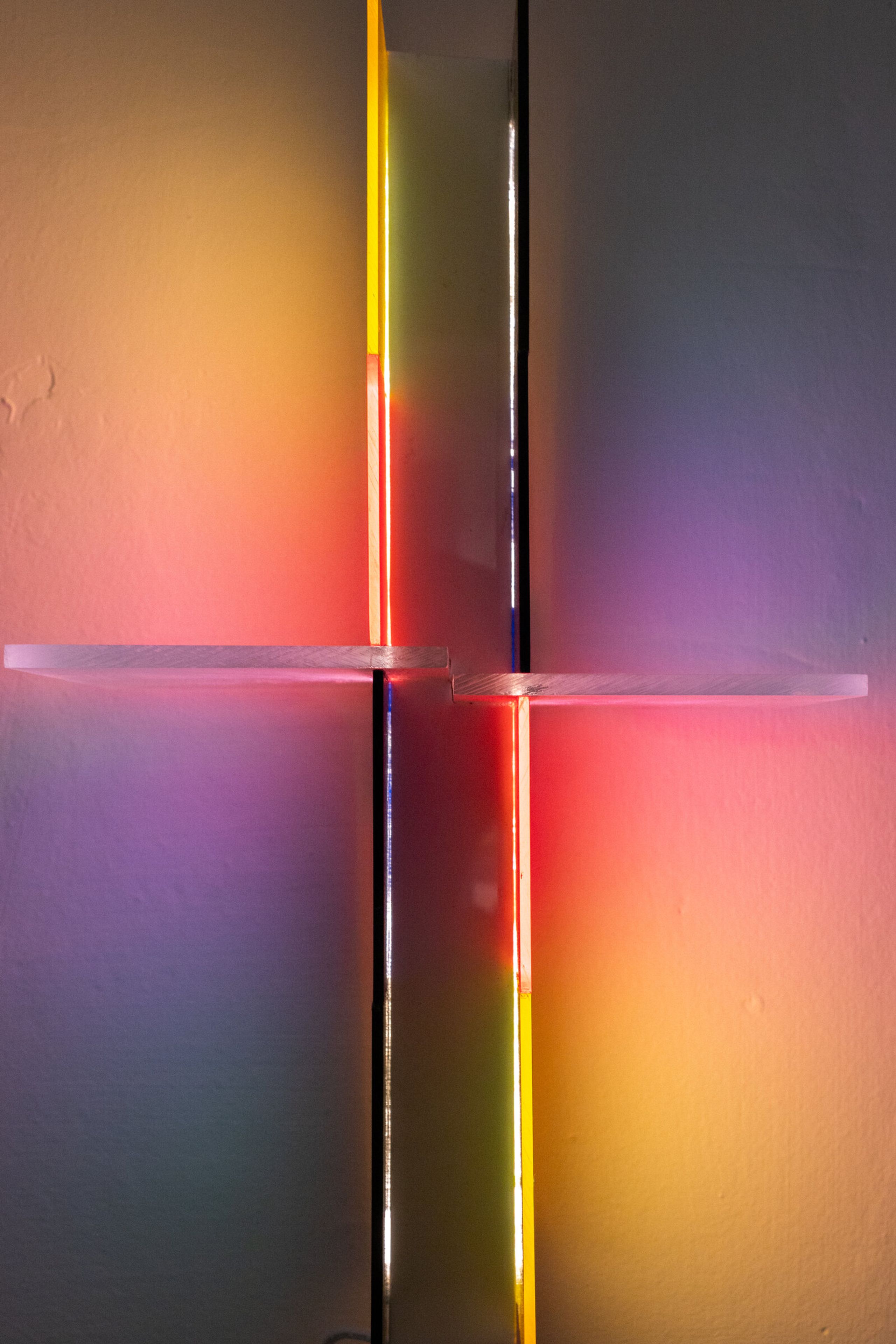Closer view of irreversible's center: a bright vertical streak with yellow on one side and red on the other, a horizontal acrylic shelf at the crossing, halos washing the wall behind