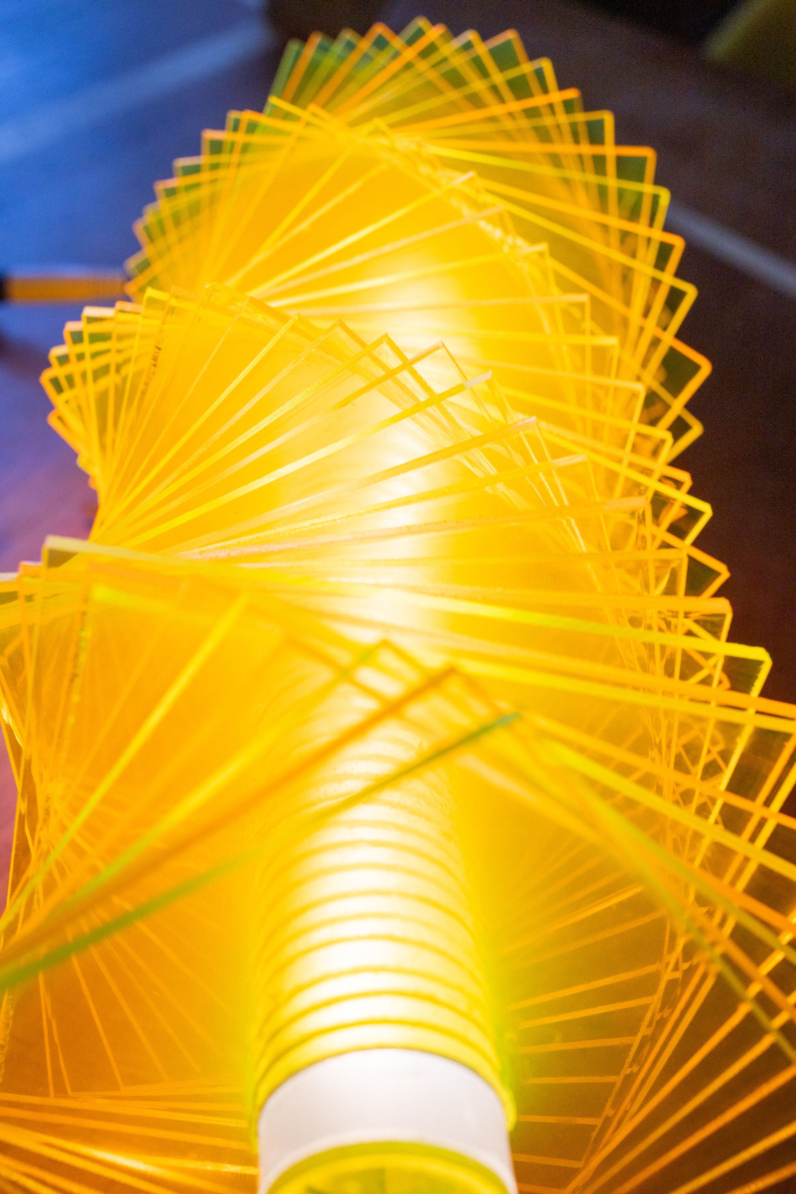 Vertical close-up of radiator IV: looking along the LED tube, fluorescent green and yellow plates spiraling outward, cut edges catching the light