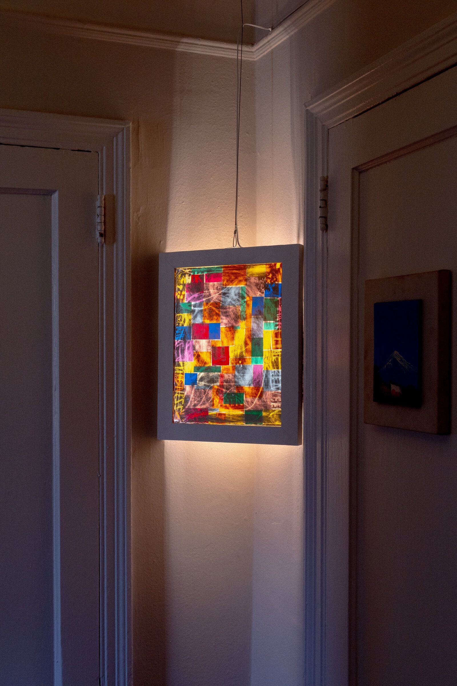 Head-on view of genius madness mirror: a small framed piece lit from above, a grid of colored squares in red, yellow, blue, green, pink, and orange visible through scratched white gesture