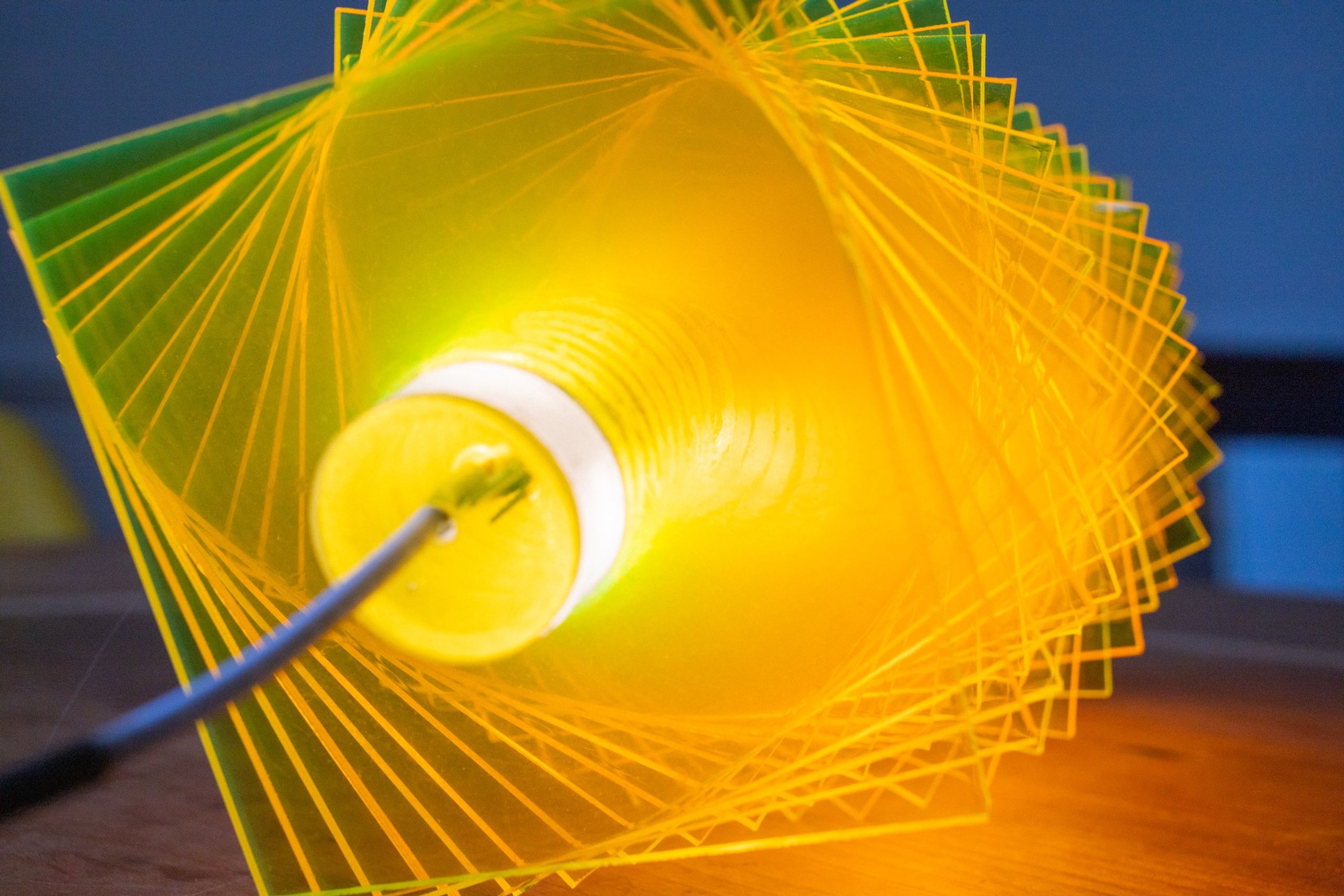 End detail of radiator IV: the LED tube and ceramic socket visible at one end, cord running off, square green and yellow plates radiating outward in a tight spiral