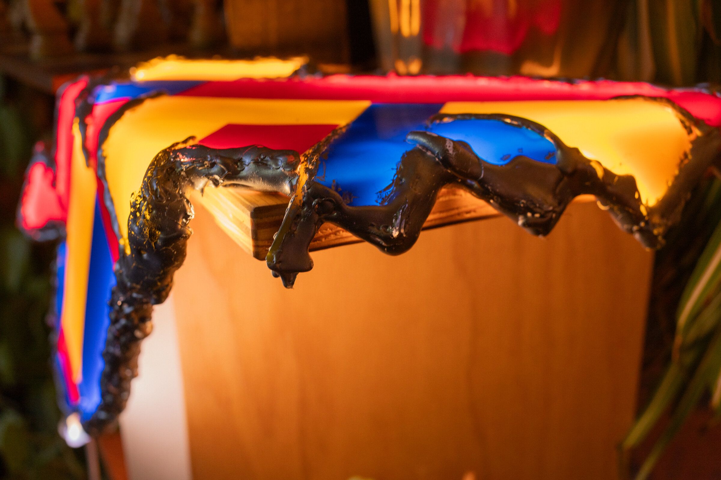 Close-up of shelf life's edge: hot glue painted silver, irregular and molten-looking, colored panels visible behind