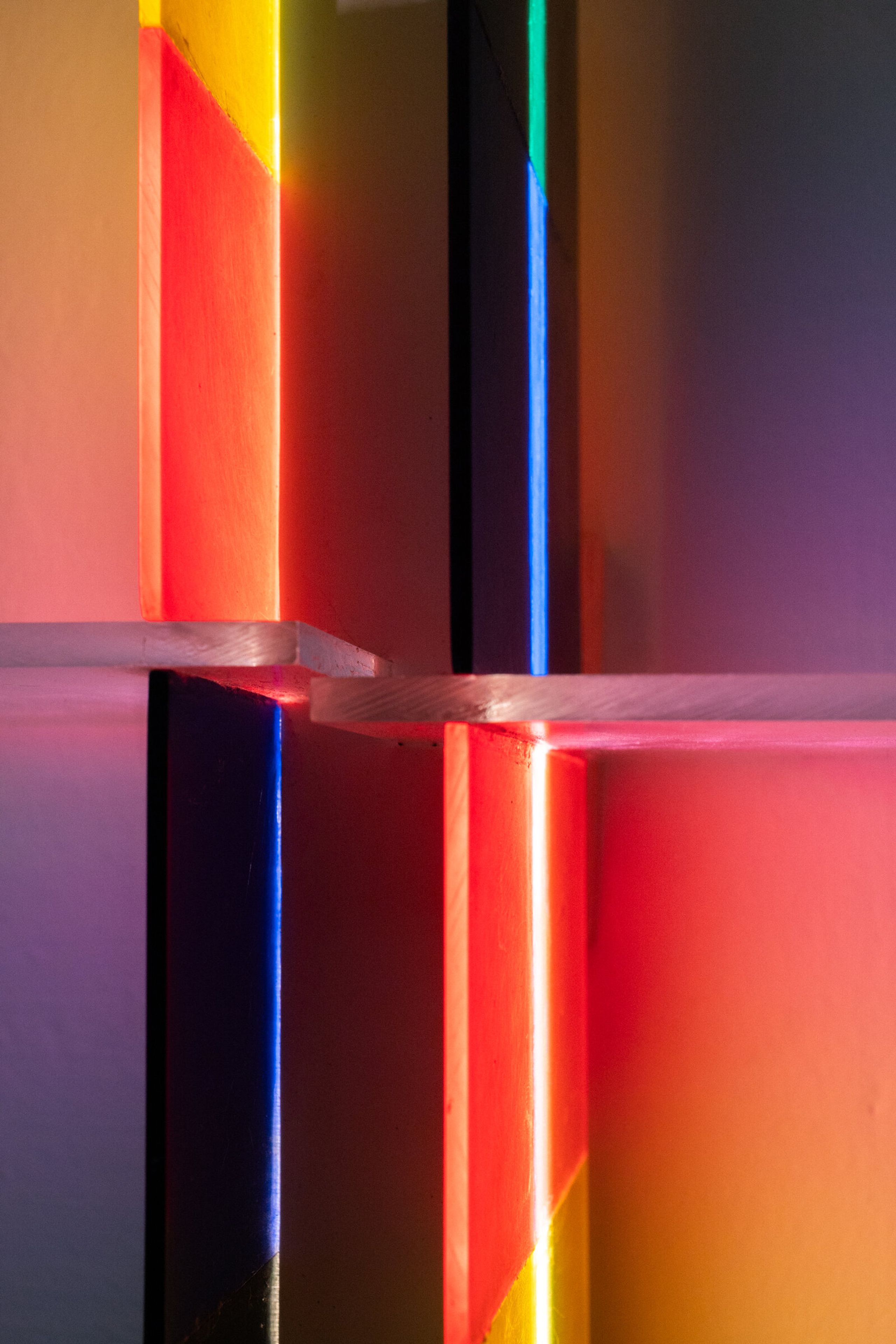 Close view of irreversible at the cross intersection: a horizontal acrylic shelf cuts across a bright vertical streak, colored panels in warm and cool pairs around it