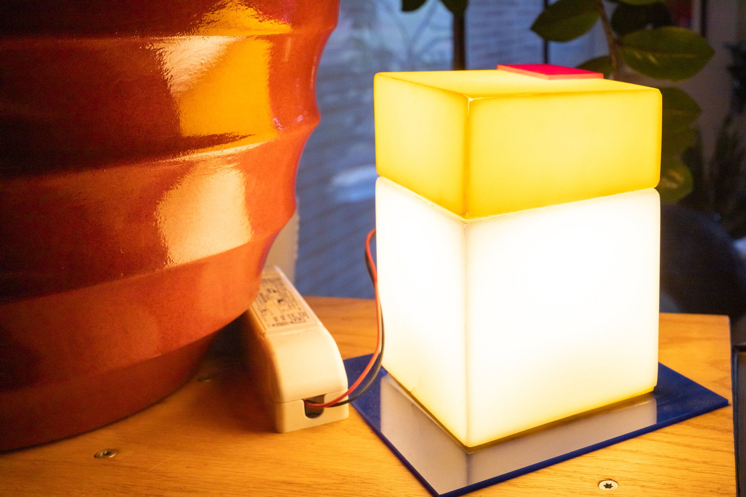 Parts and all from a side angle: a yellow cap on top of a frosted white cube, blue plate beneath, a small red square offset on the cap