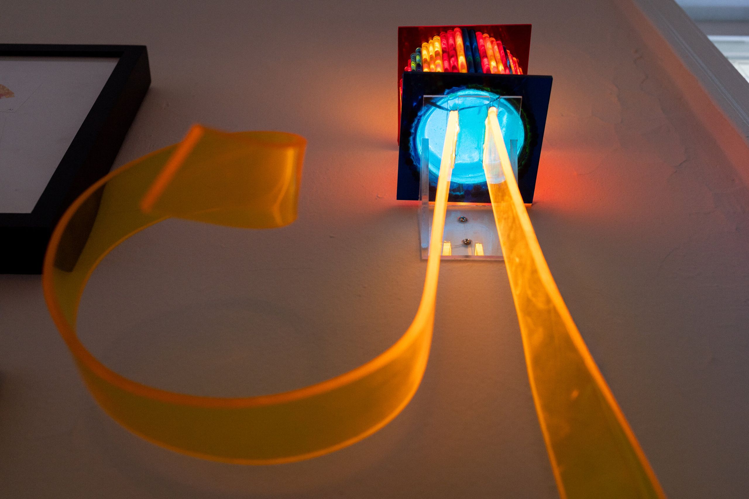 Low angled view of i've been thinking about flowers from below: a blue circular element visible on the underside of the box, the orange tendrils descending past the camera