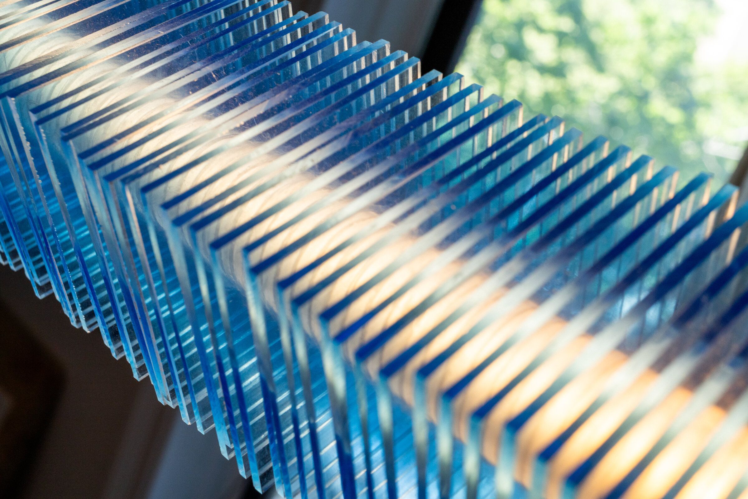 Diagonal close-up of radiator I: parallel blue plates with warm light running between them, daylight from a window beyond
