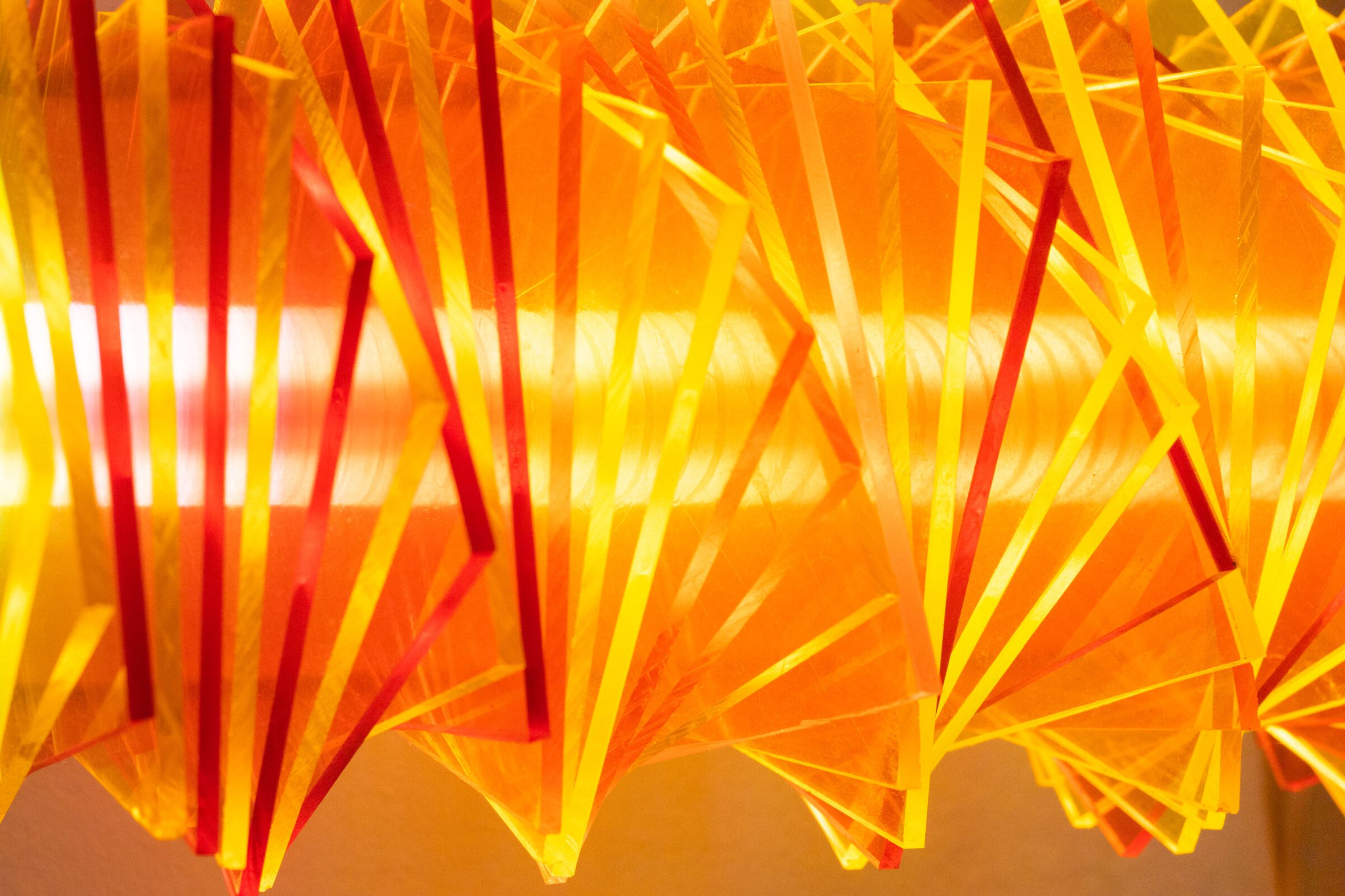 Closer side view of radiator II: red, yellow, and orange plates stacked irregularly against each other, the warm filament running horizontally through their center