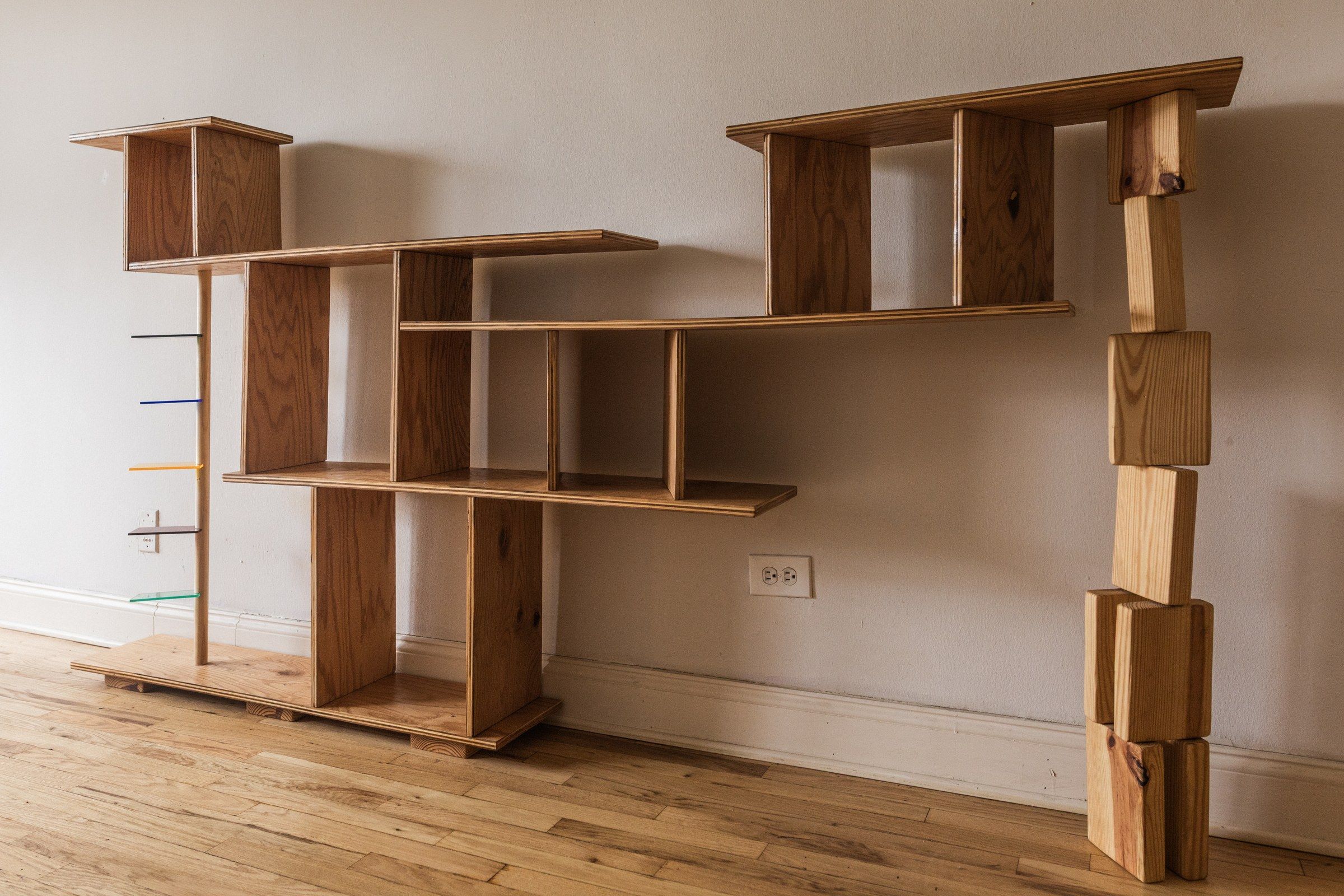 The wooden shelf beside a dark sofa, lit warm in the corner of a room.