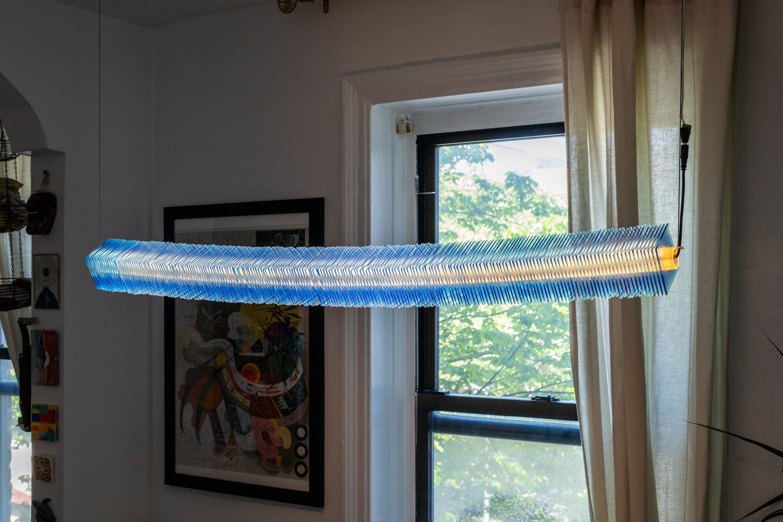 Side view of radiator I from below: the stack of blue plates reads as a thin horizontal line, the warm interior visible as a continuous orange band running its full length