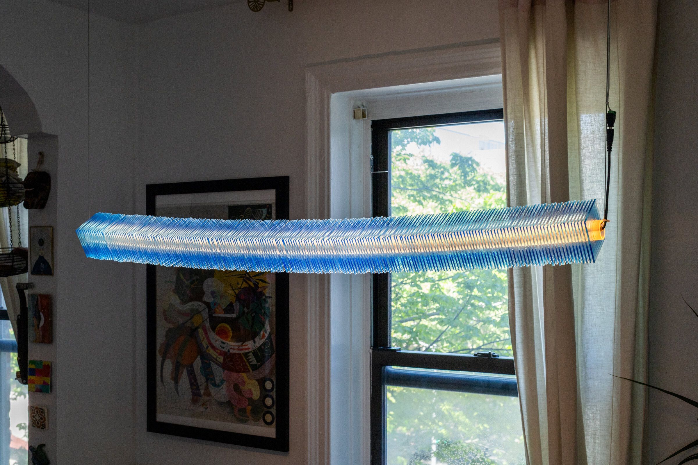 Side view of radiator I from below: the stack of blue plates reads as a thin horizontal line, the warm interior visible as a continuous orange band running its full length